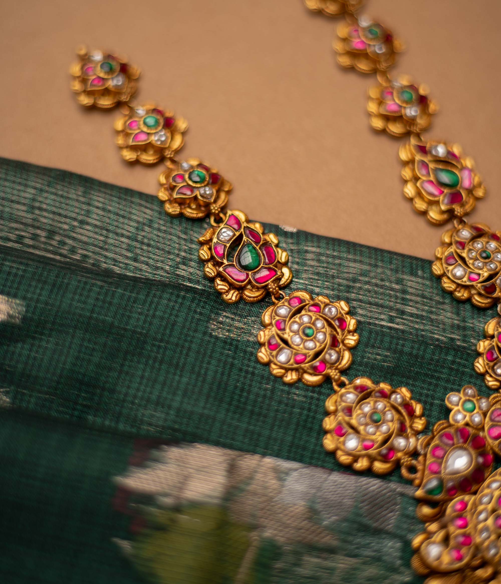 Close-up of a Kundan necklace with pearls and gems. The necklace is displayed on a brown bust against a blurred background.
