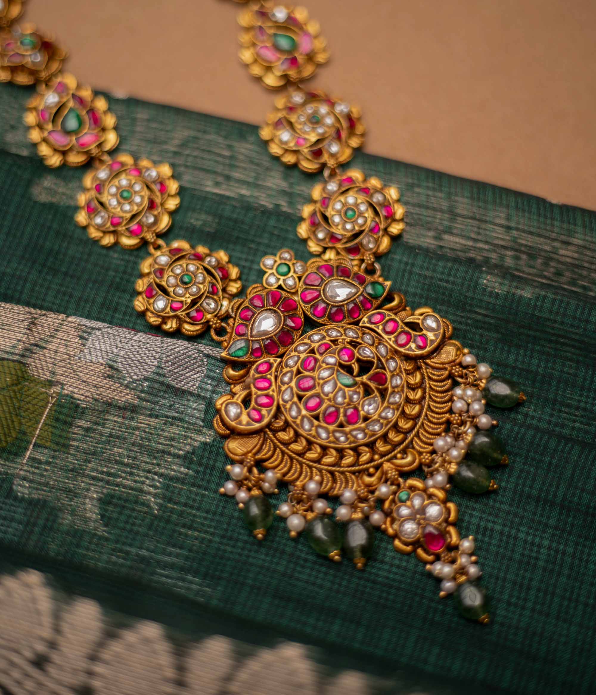 Close-up of a Kundan necklace with pearls and gems. The necklace is displayed on a brown bust against a blurred background.