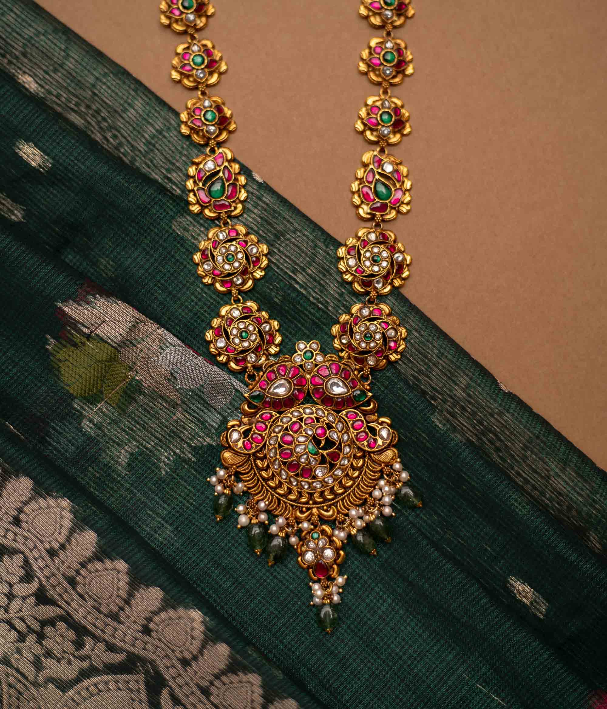 Close-up of a Kundan necklace with pearls and gems. The necklace is displayed on a brown bust against a blurred background.