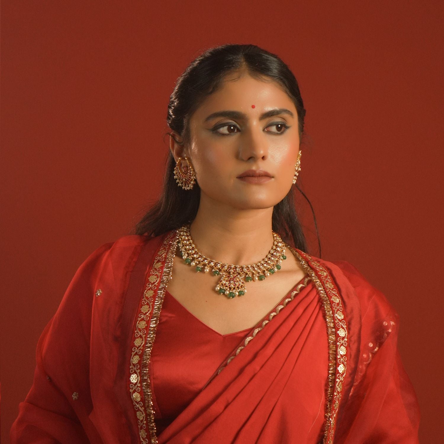 Woman in traditional red attire with jewelry against a red background