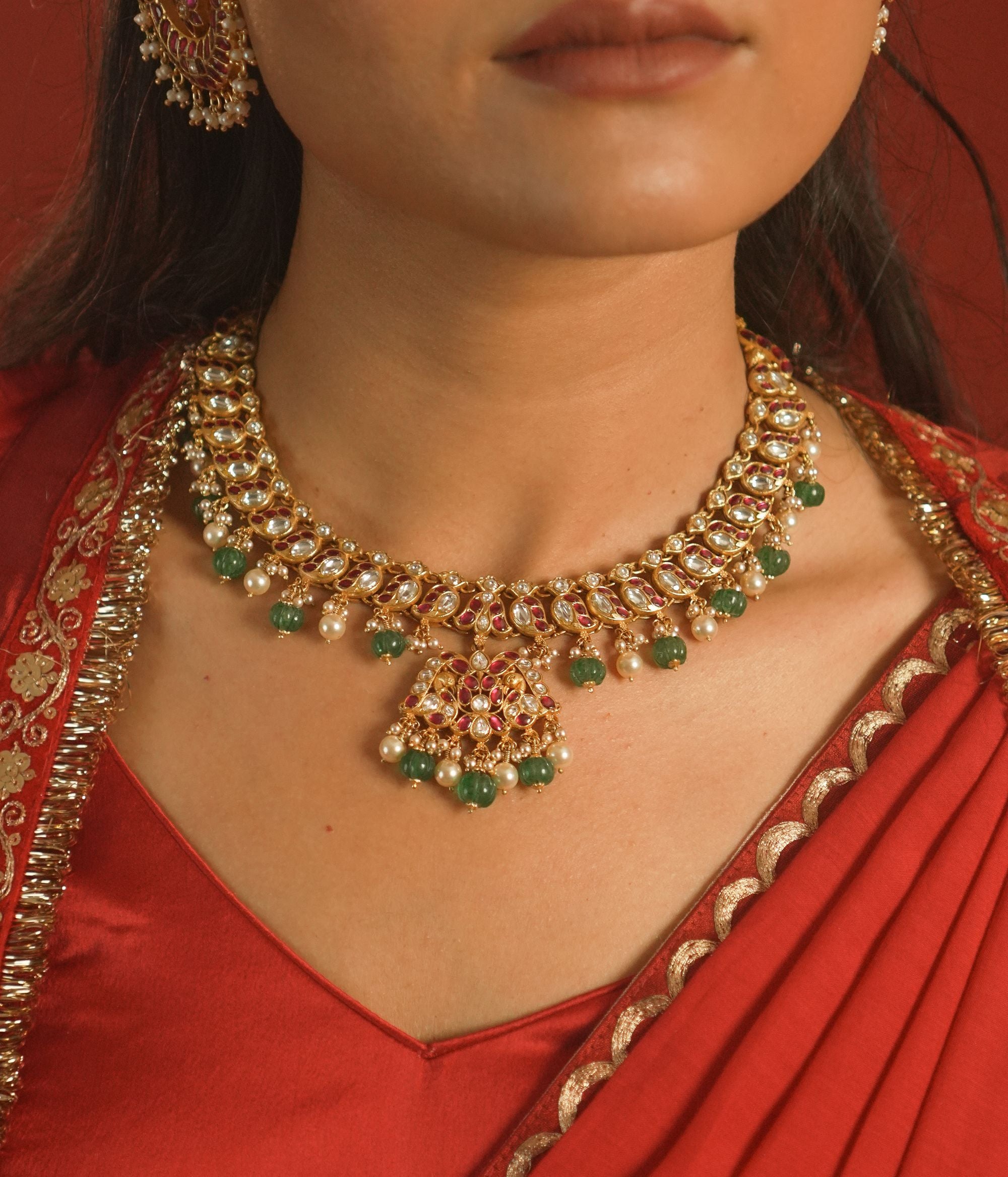 Gold necklace with green stones worn by a person in a red outfit.
