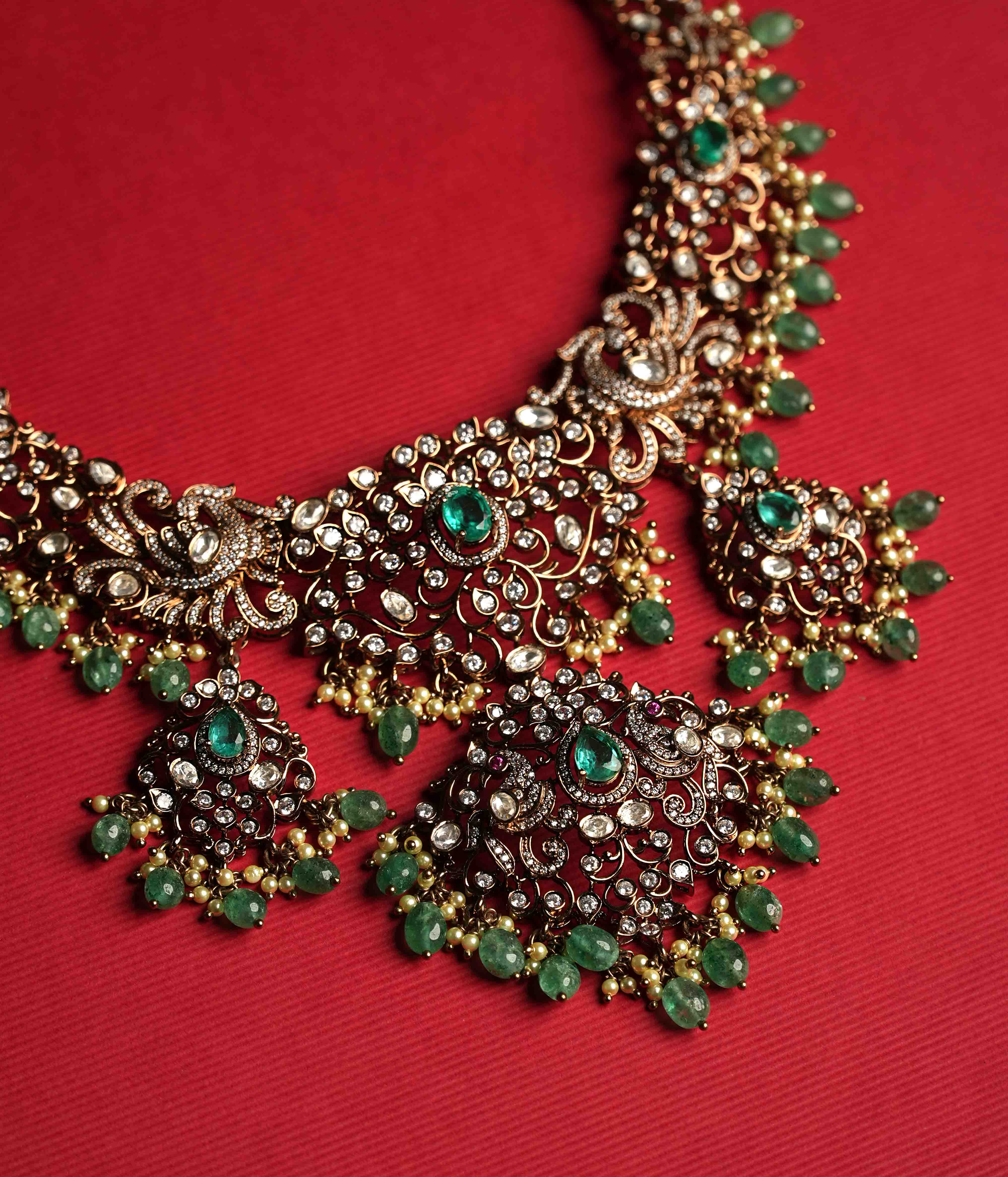 An elaborate moissanite necklace handcrafted from 92.5 sterling silver with 14ct dark antique gold plating, featuring CZ stones, a green gemstone, polki stones, and pearls, finished in a Victorian style, with cultured emerald and pearl dangles evoking vintage luxury.
