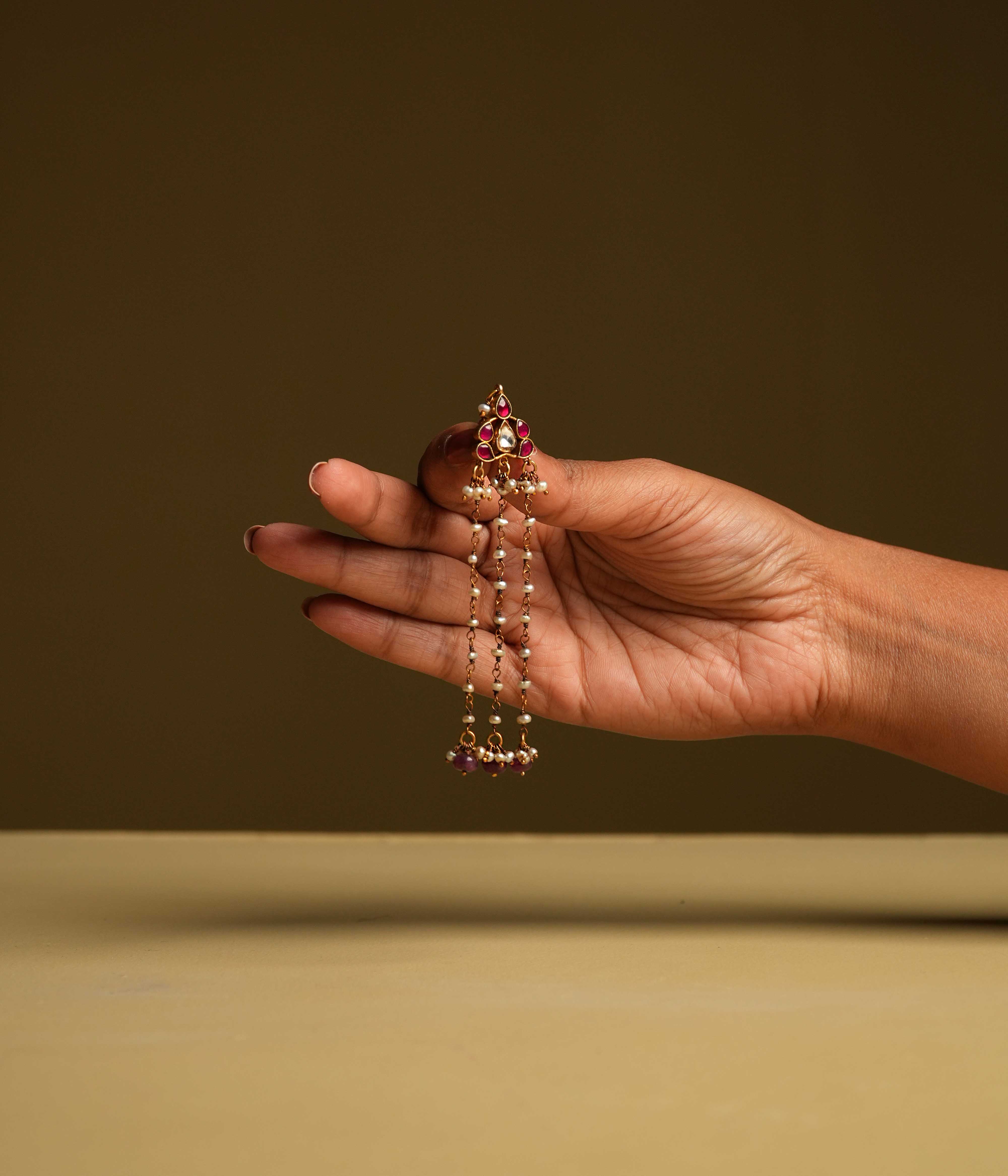 Keshini Earrings made of 92.5 sterling silver with screw-type fastening. Featuring red and white Kundan stones, red beads, and pearls, this exquisite pair exudes celestial elegance and timeless charm, designed for the woman who captivates with every glance.