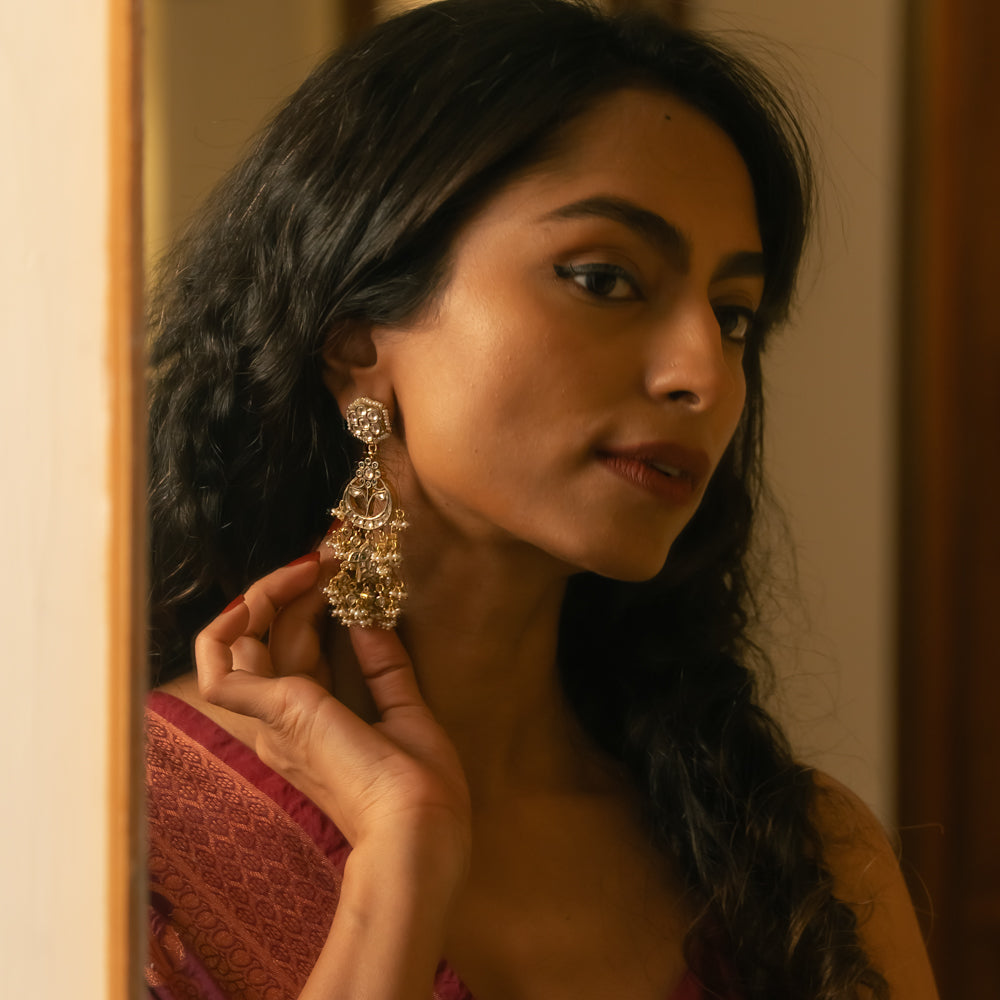 Woman wearing ornate gold Taarini earrings with rubies, white sapphires, and pearl danglers.