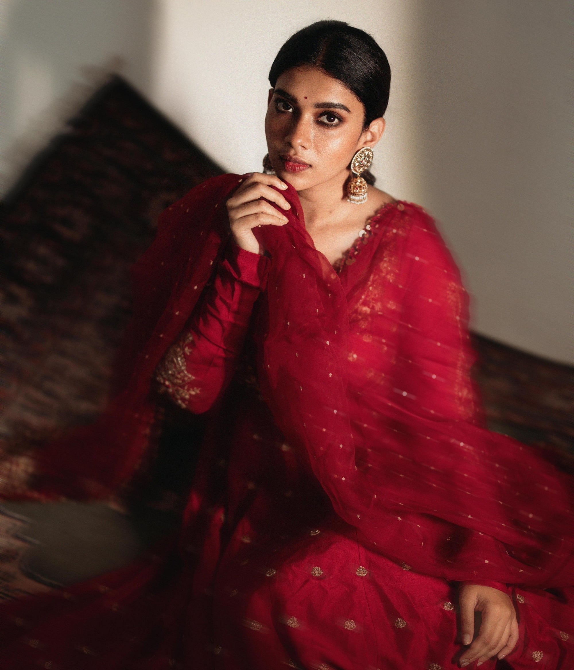 Large gold jhumka earrings with white sapphires, rubies, and pearls, on a woman wearing a red sari.