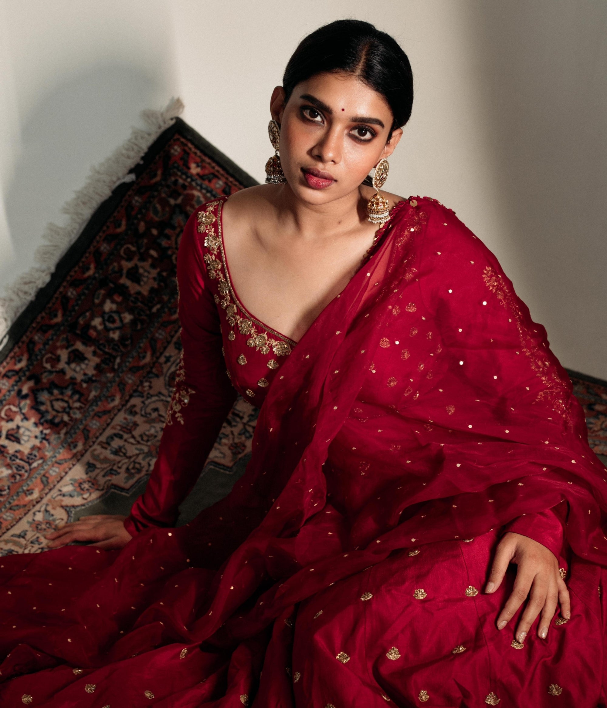 Large gold jhumka earrings with white sapphires, rubies, and pearls, on a woman wearing a red sari.