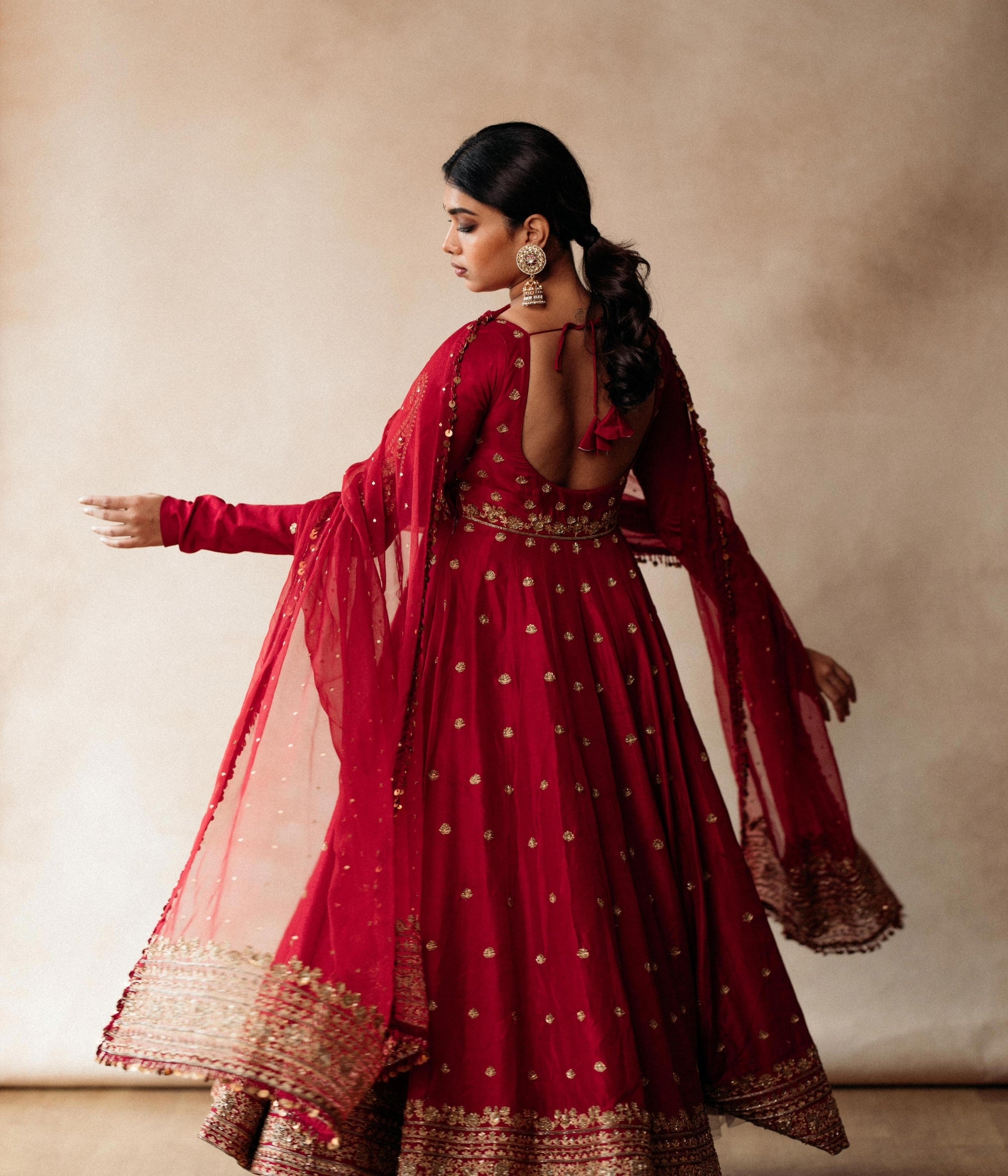 Large gold jhumka earrings with white sapphires, rubies, and pearls, on a woman wearing a red sari.