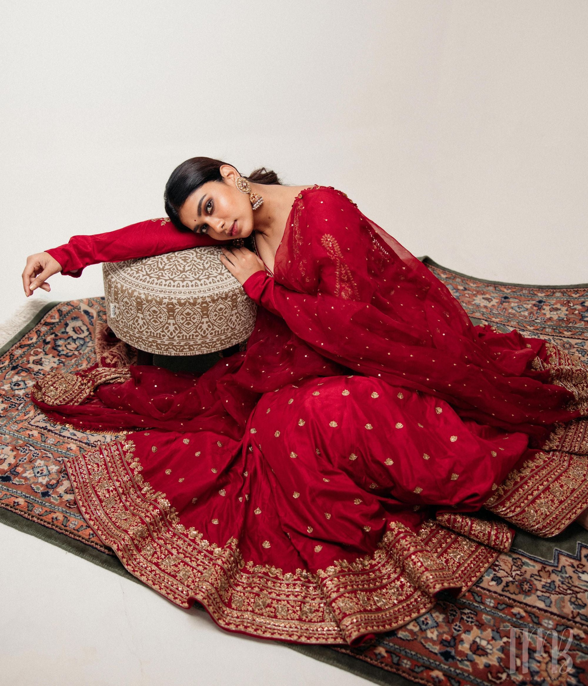 Large gold jhumka earrings with white sapphires, rubies, and pearls, on a woman wearing a red sari.