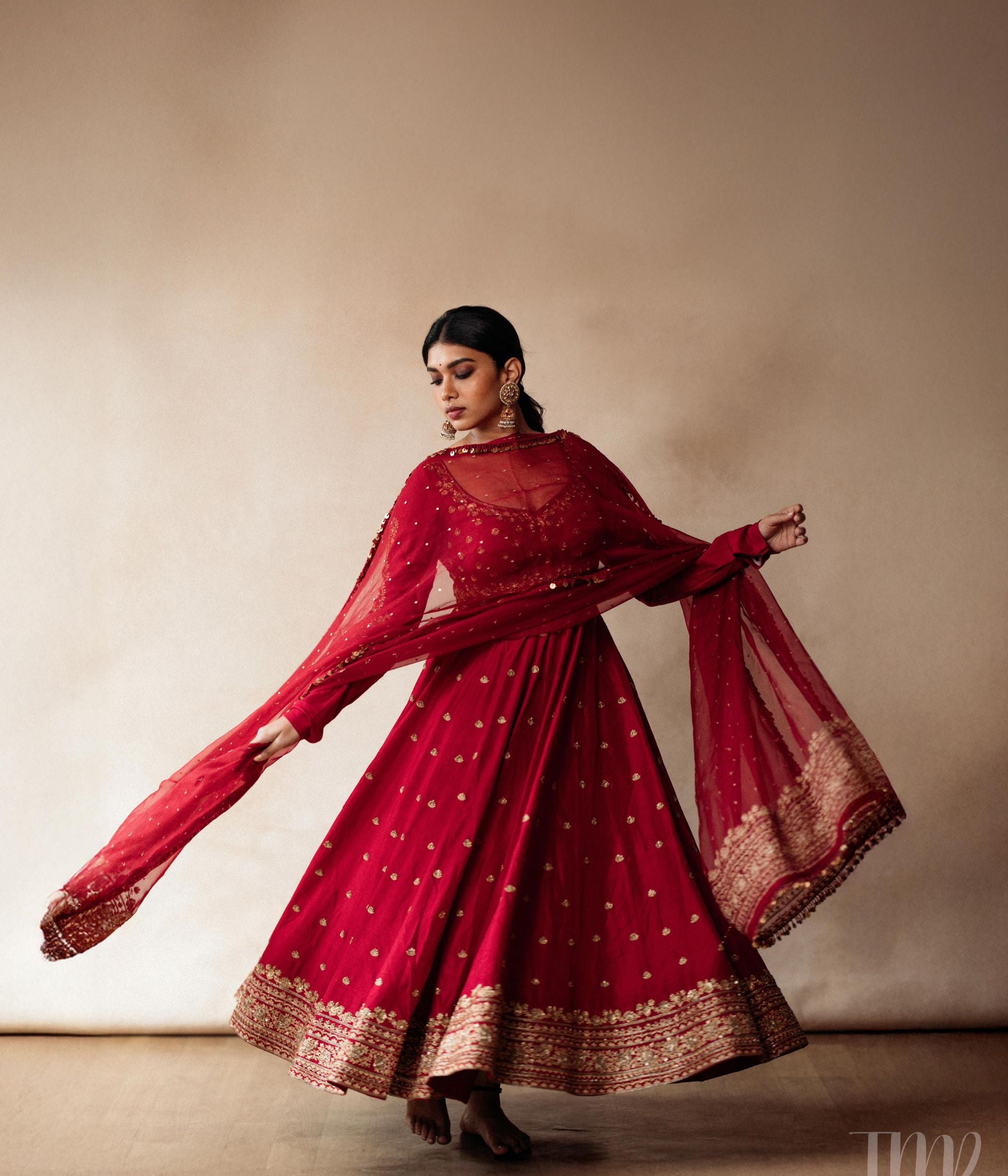 Large gold jhumka earrings with white sapphires, rubies, and pearls, on a woman wearing a red sari.