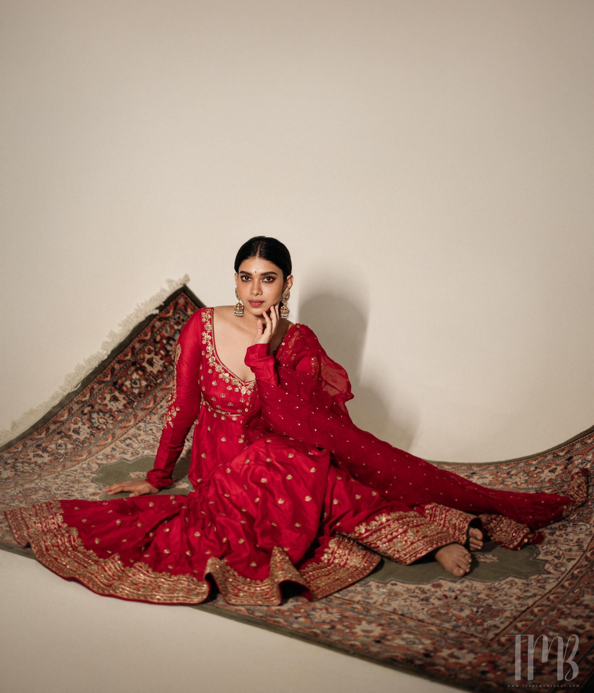 Large gold jhumka earrings with white sapphires, rubies, and pearls, on a woman wearing a red sari.