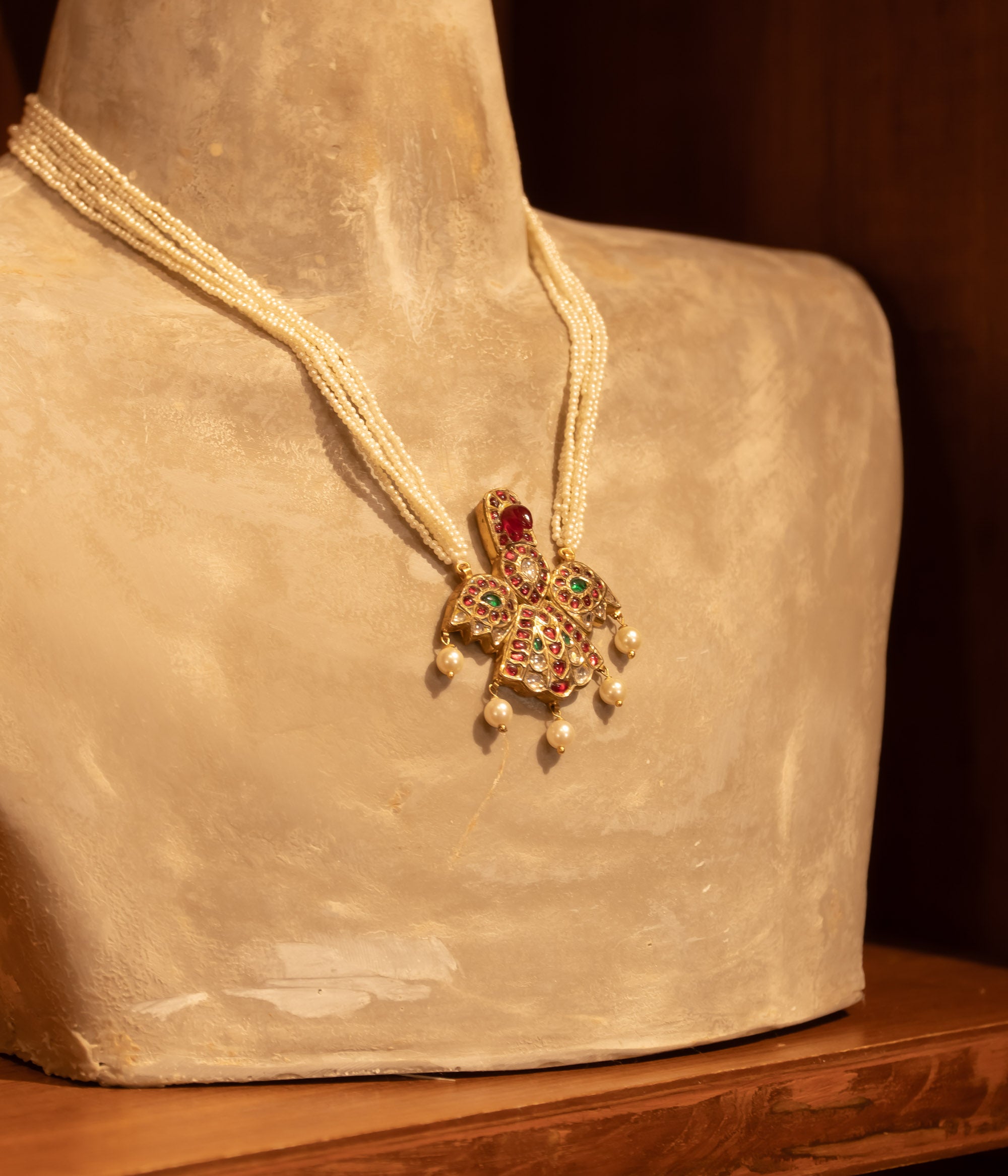 Multi-strand pearl necklace with a central gold pendant featuring rubies and white sapphires, displayed on a mannequin bust.