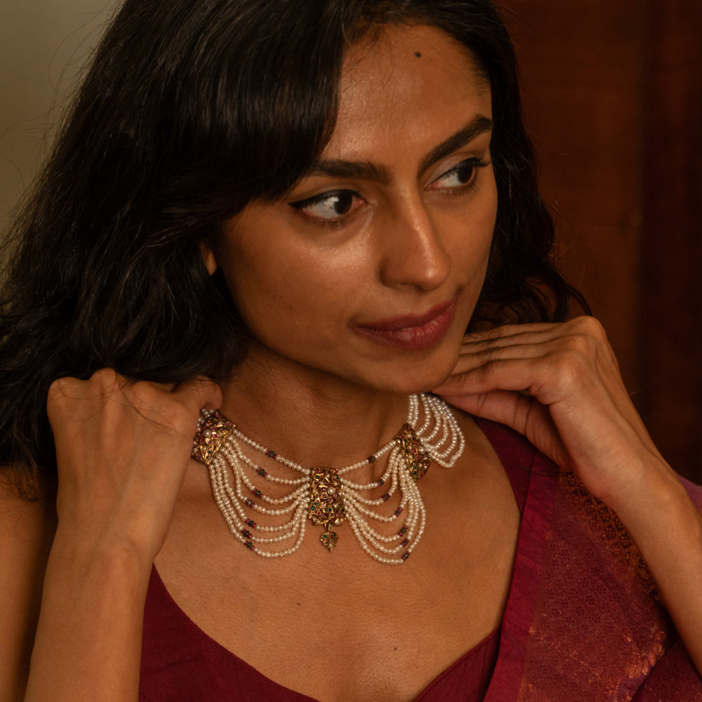 Multi-strand pearl necklace with a central gold pendant featuring rubies and white sapphires, worn by a woman.