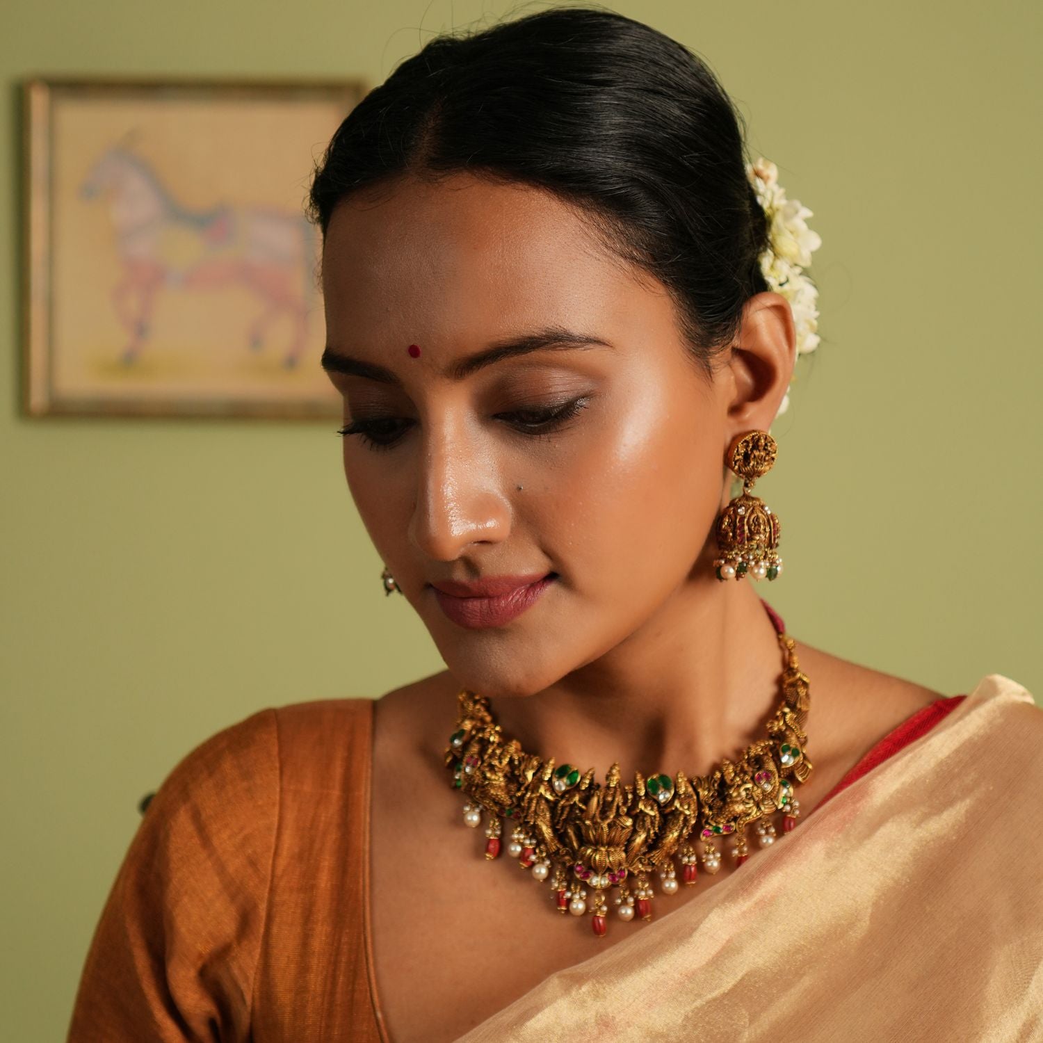 Gold-plated silver temple jewellery necklace featuring detailed carvings of Goddess Lakshmi and Lord Ganesh, adorned with red Kundan stones, white Kundan stones, white pearls, and red beads, exuding a regal and divine charm.