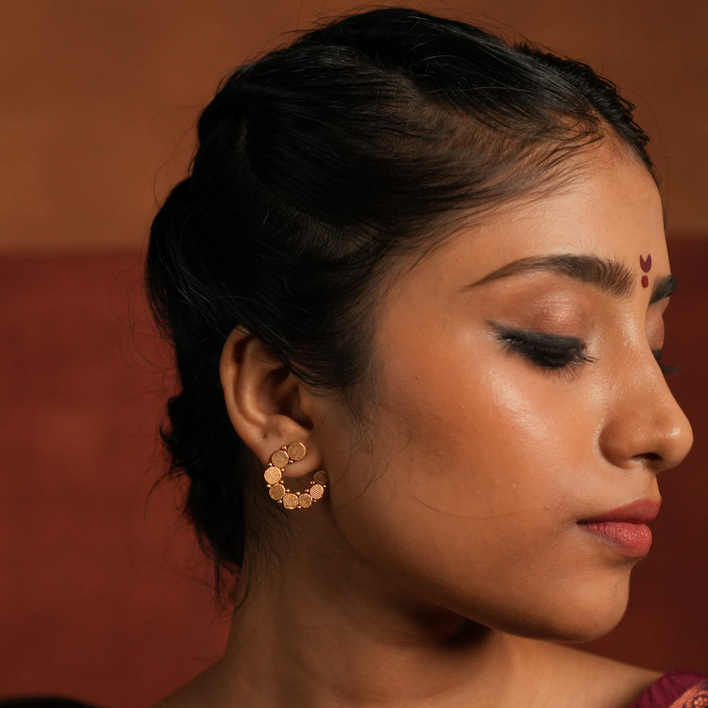 These gold-plated silver stud earrings showcase dainty coin-like motifs arranged in a graceful circular pattern. Inspired by vintage Kolhapuri tribal designs, they blend tradition with elegance, making them a timeless addition to any jewelry collection.