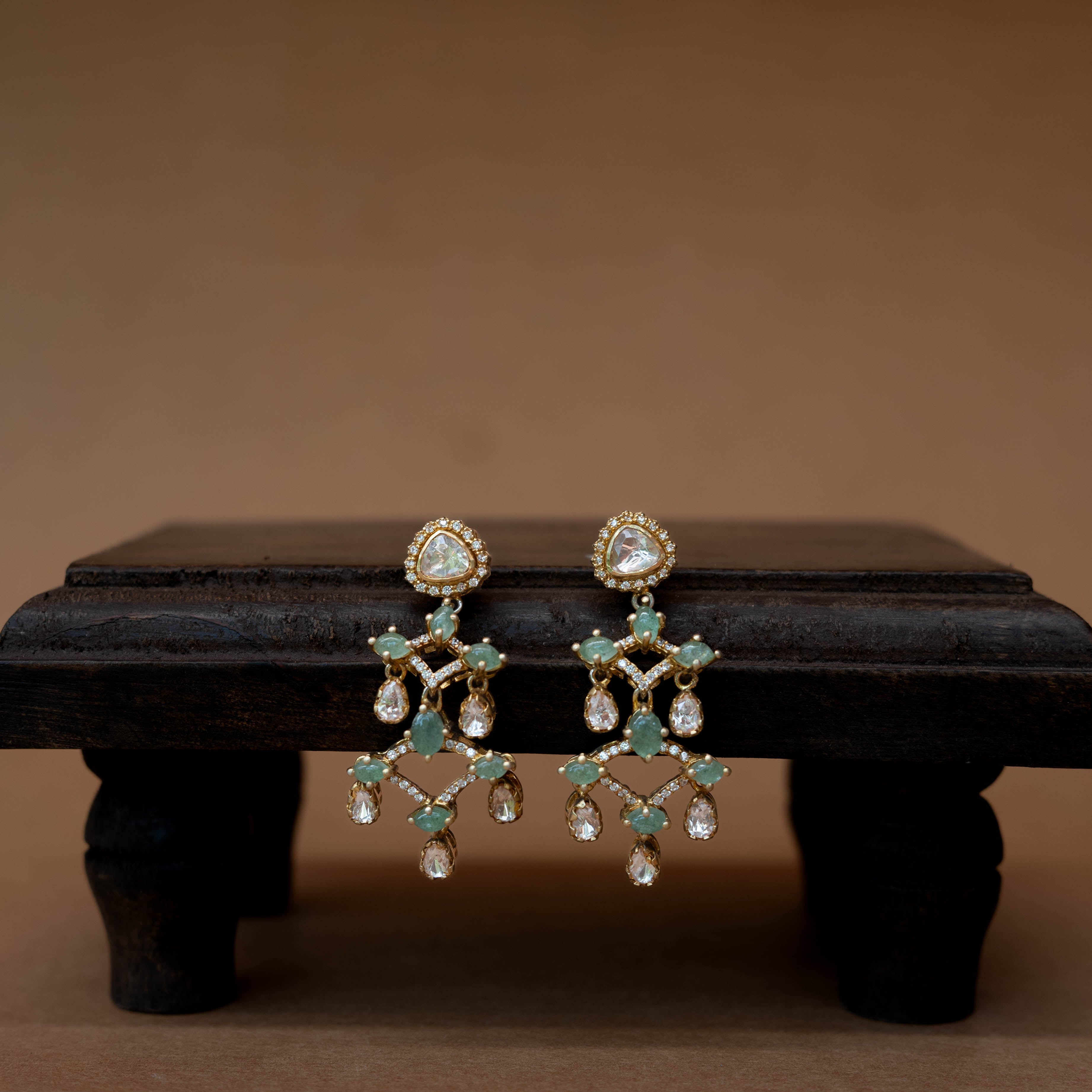 Intricate floral earrings with a central green stone, surrounded by clear stones.