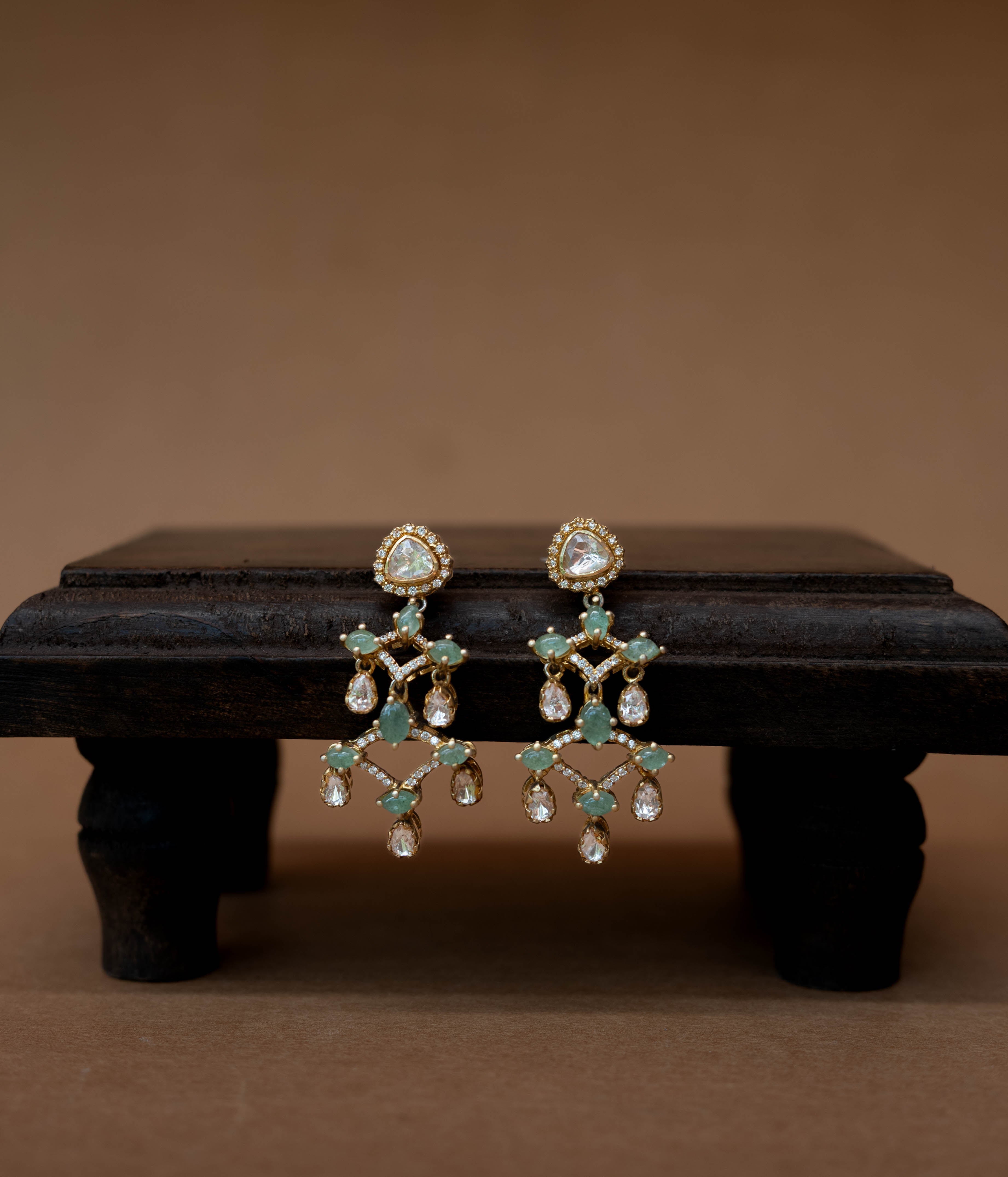 Intricate floral earrings with a central green stone, surrounded by clear stones.