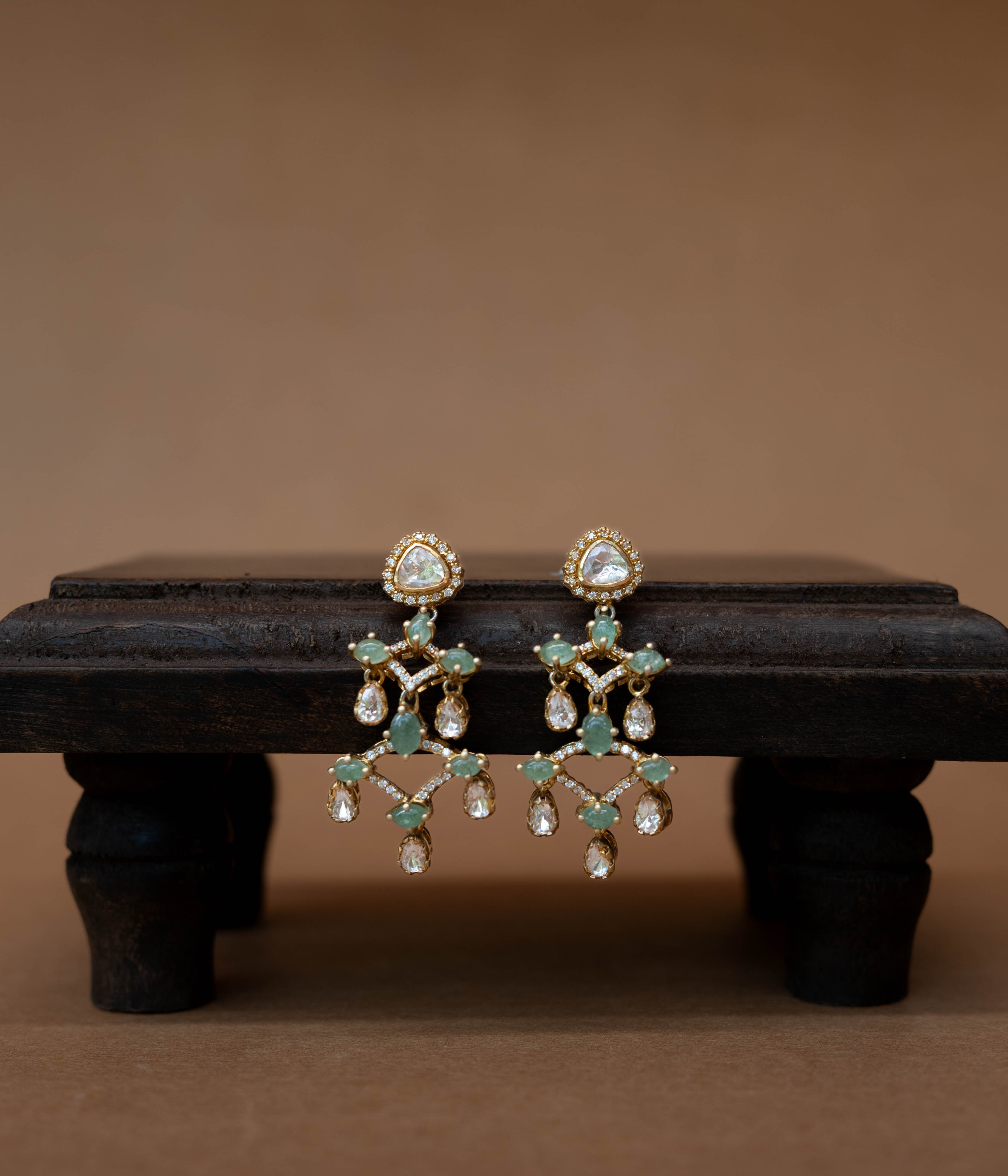 Intricate floral earrings with a central green stone, surrounded by clear stones.