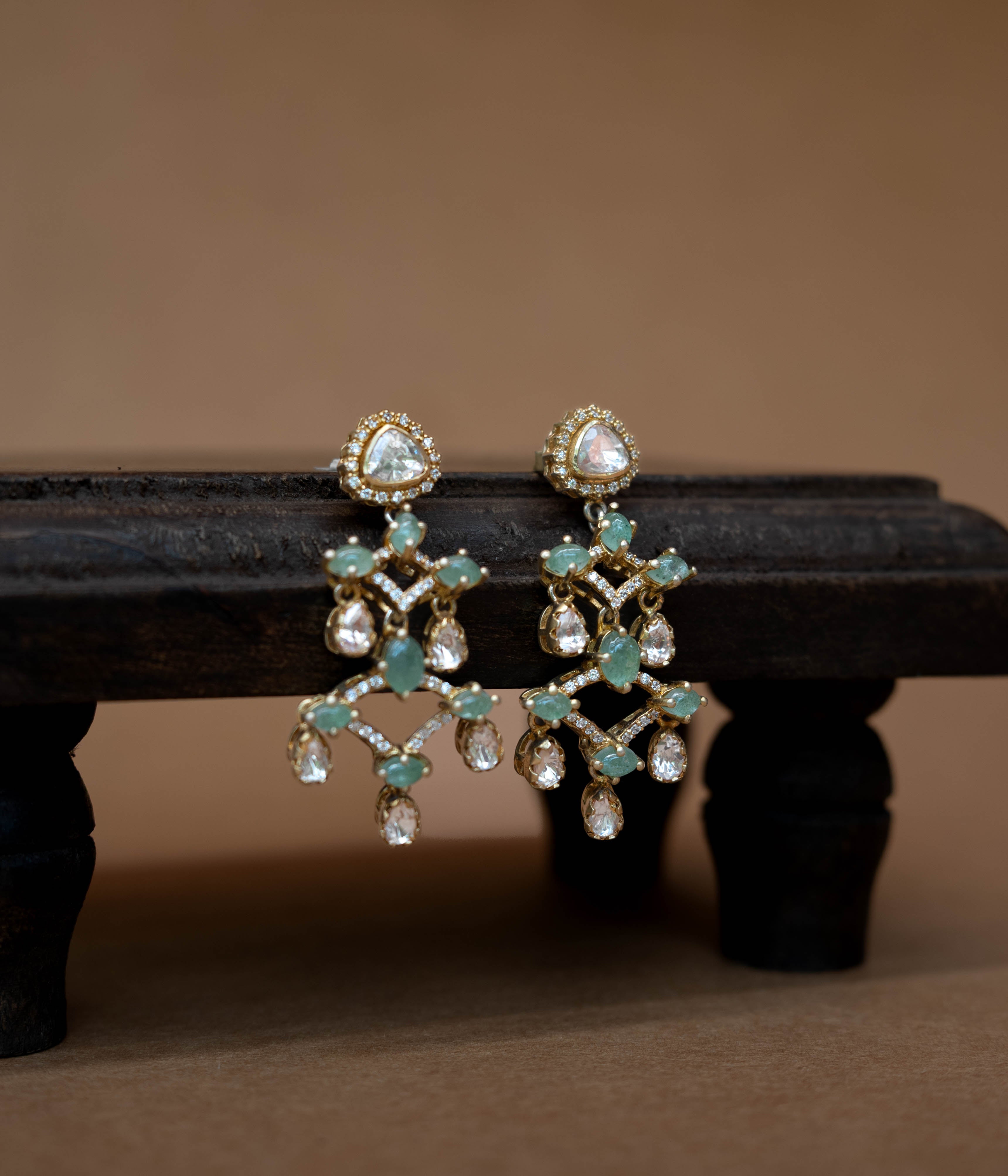 Intricate floral earrings with a central green stone, surrounded by clear stones.