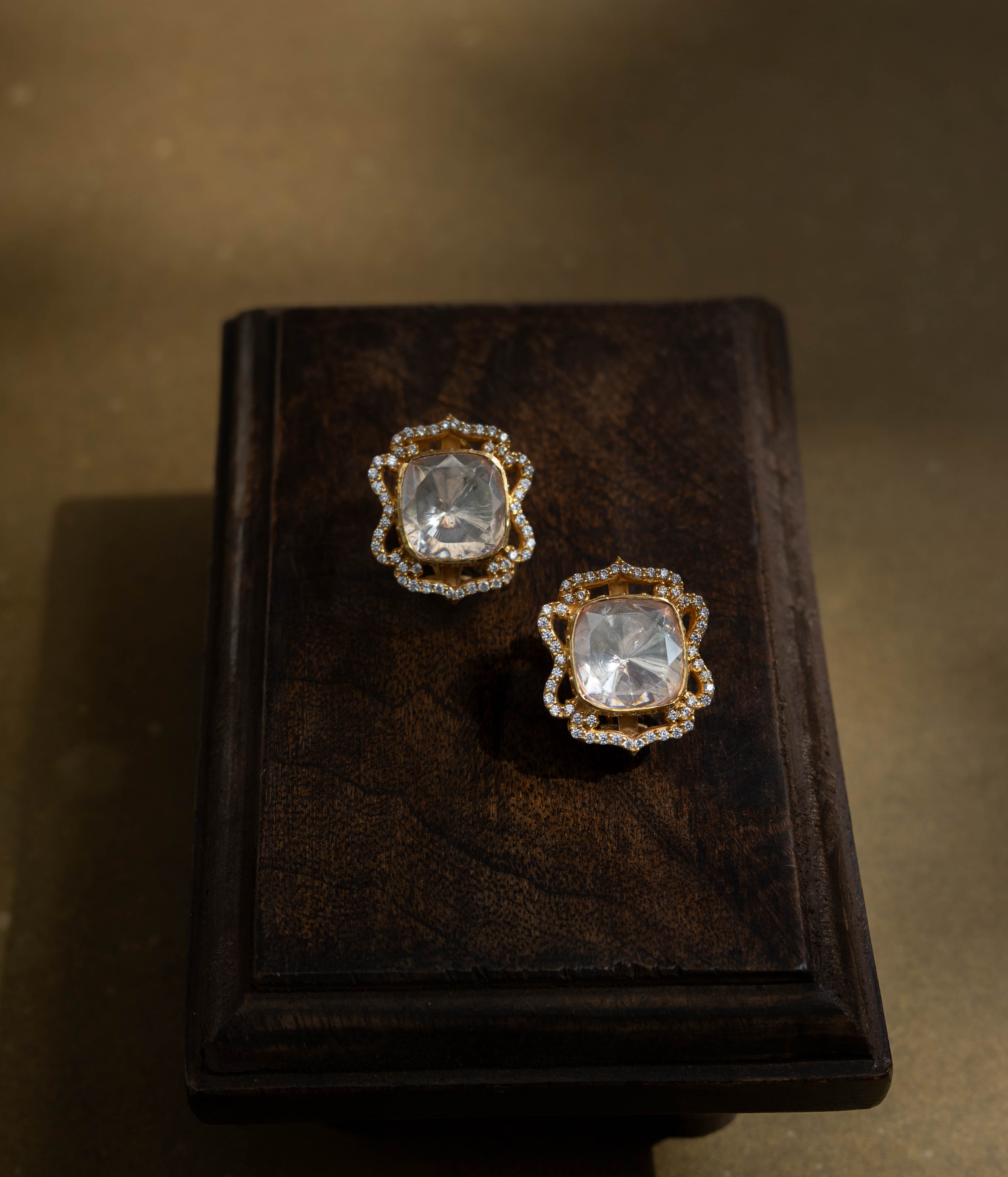 Large, intricate earrings with a studded top and a dangling motif, all set with clear stones.
