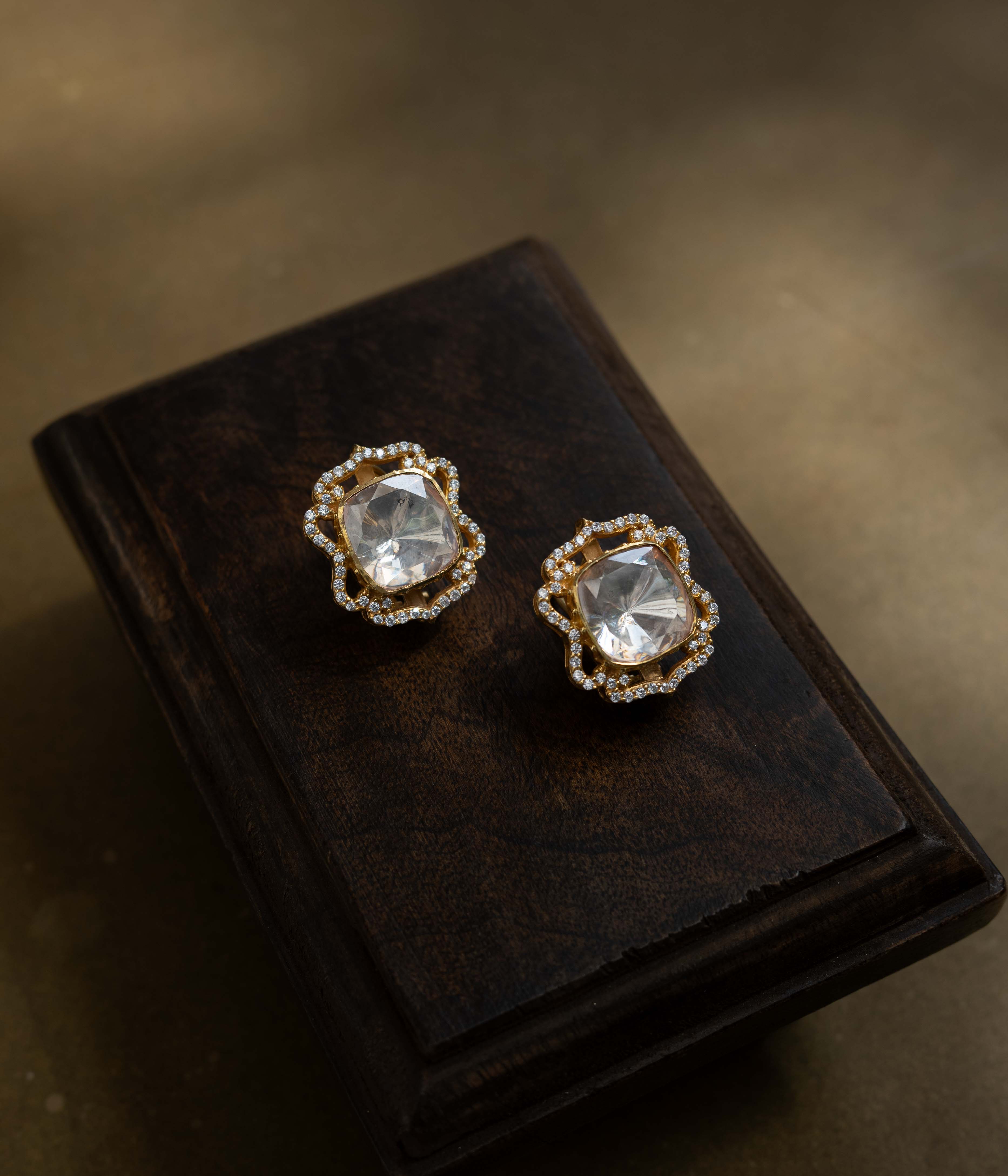 Large, intricate earrings with a studded top and a dangling motif, all set with clear stones.
