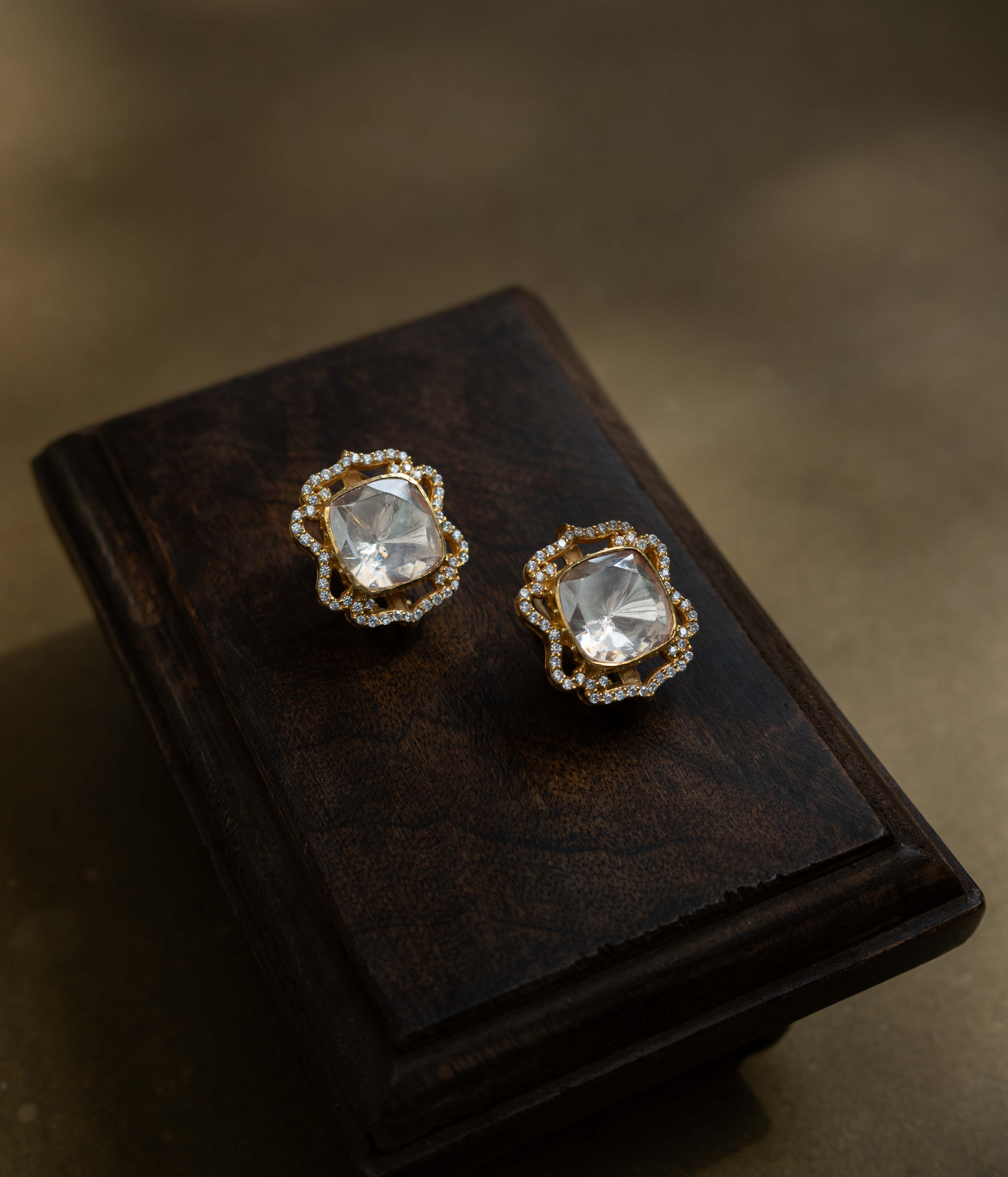 Large, intricate earrings with a studded top and a dangling motif, all set with clear stones.
