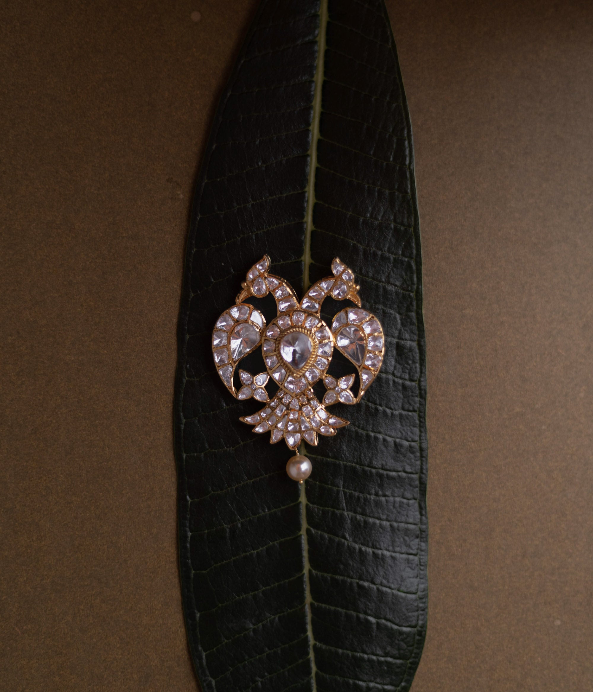 Antique gold pendant featuring twin peacocks, set with moissanite polki stones, and a single pearl drop.