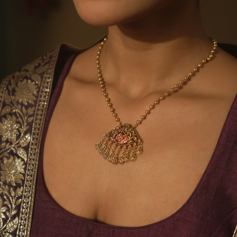 Gold necklace with a teardrop pendant with a central red gem and filigree.