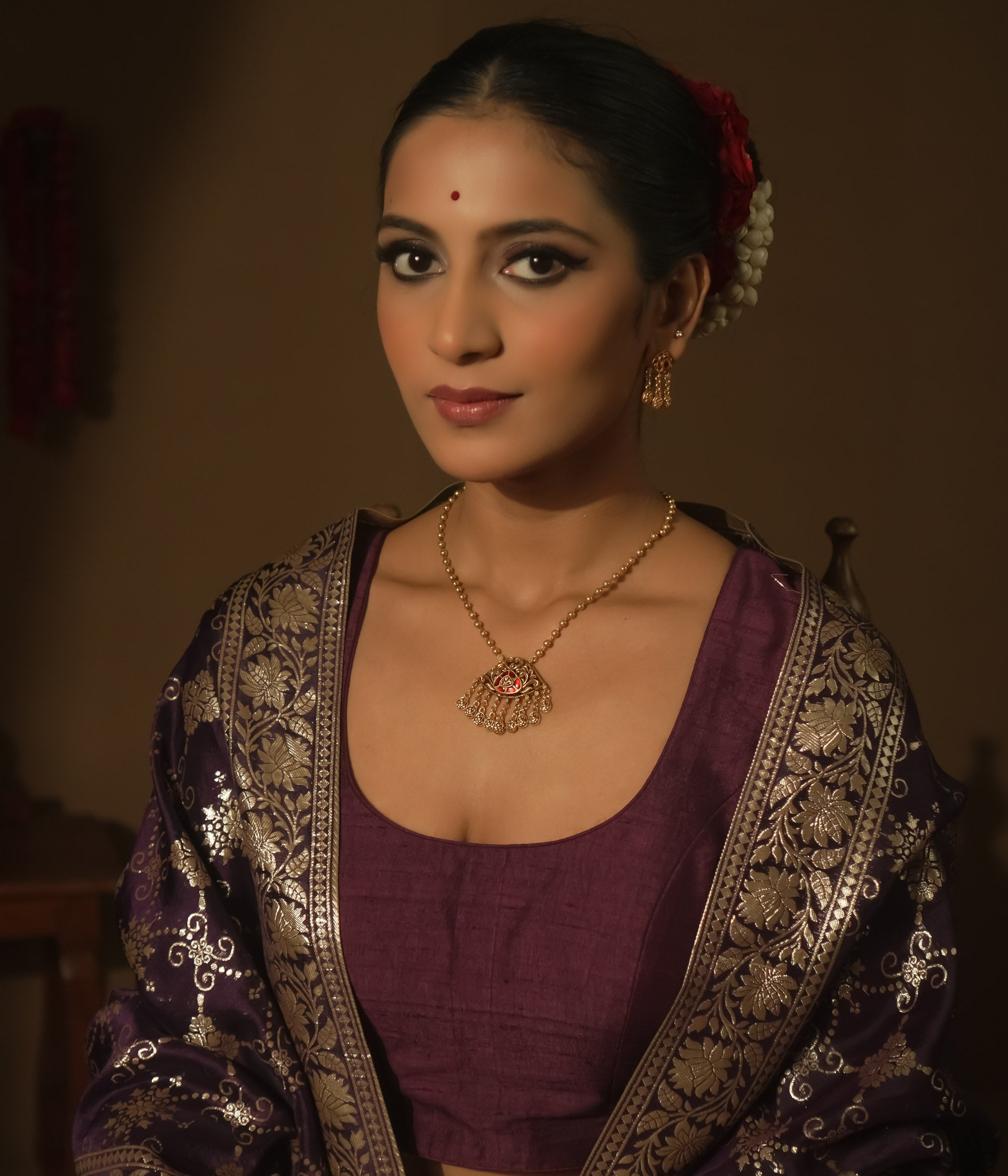 Gold necklace with a teardrop pendant with a central red gem and filigree.
