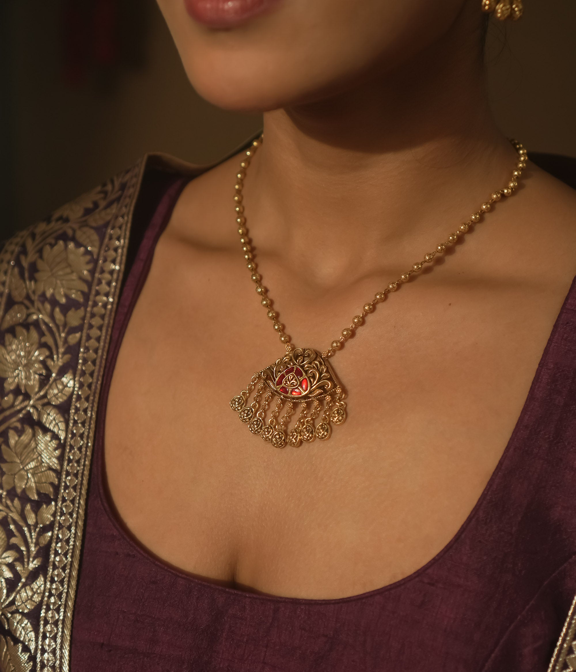 Gold necklace with a teardrop pendant with a central red gem and filigree.