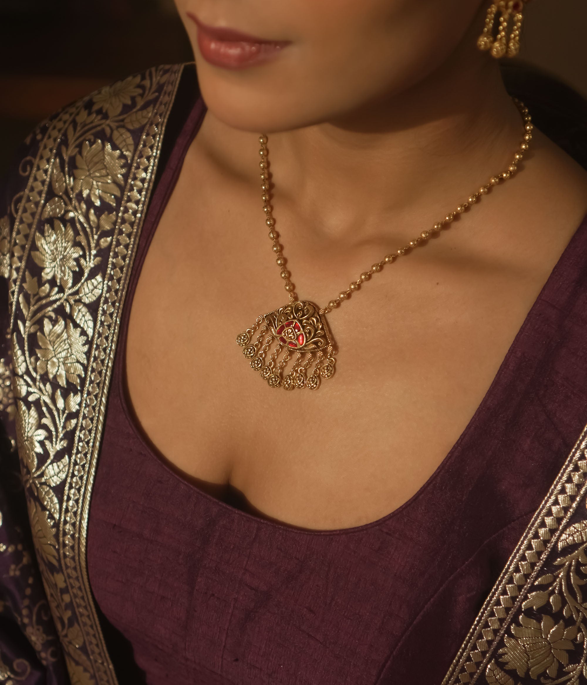 Gold necklace with a teardrop pendant with a central red gem and filigree.