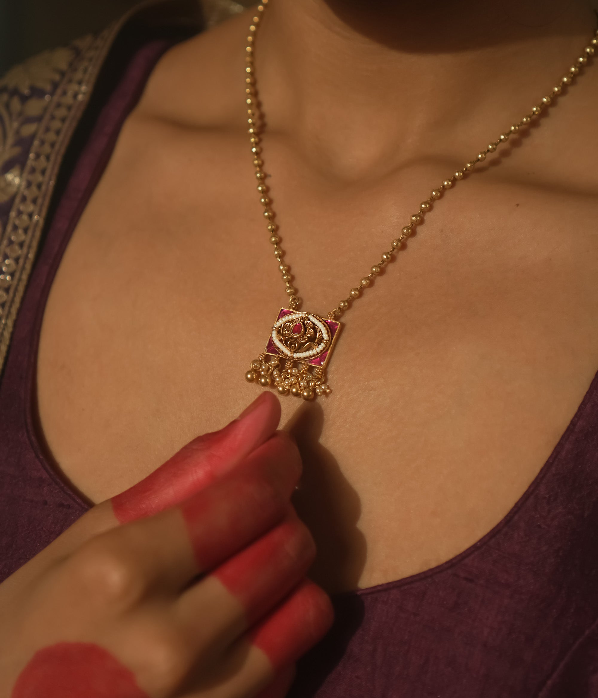 Necklace with gold beads and a square pendant with pink gemstones and gold filigree.