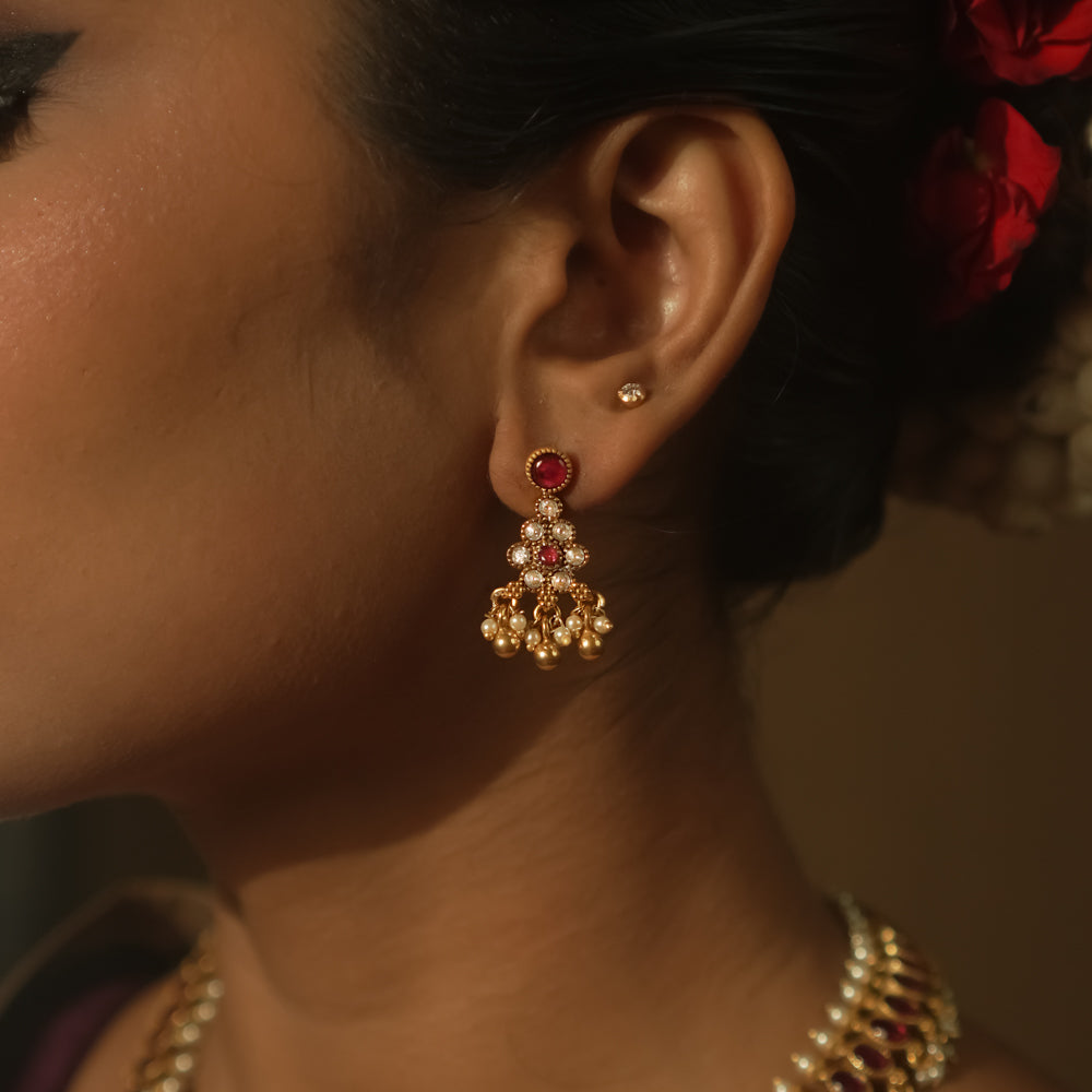 A red ear stud paired with a dangling gold jhumka with beads and gems.