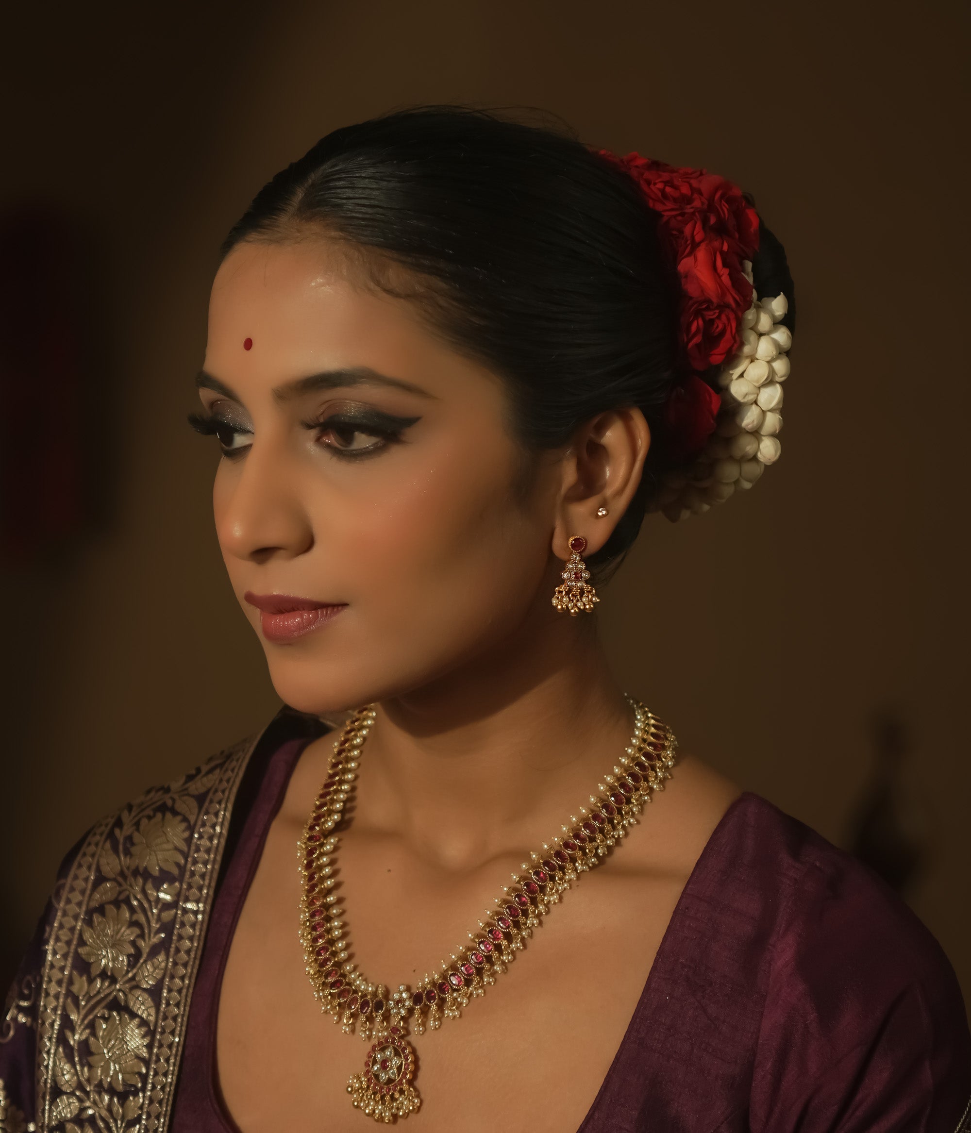 A red ear stud paired with a dangling gold jhumka with beads and gems.