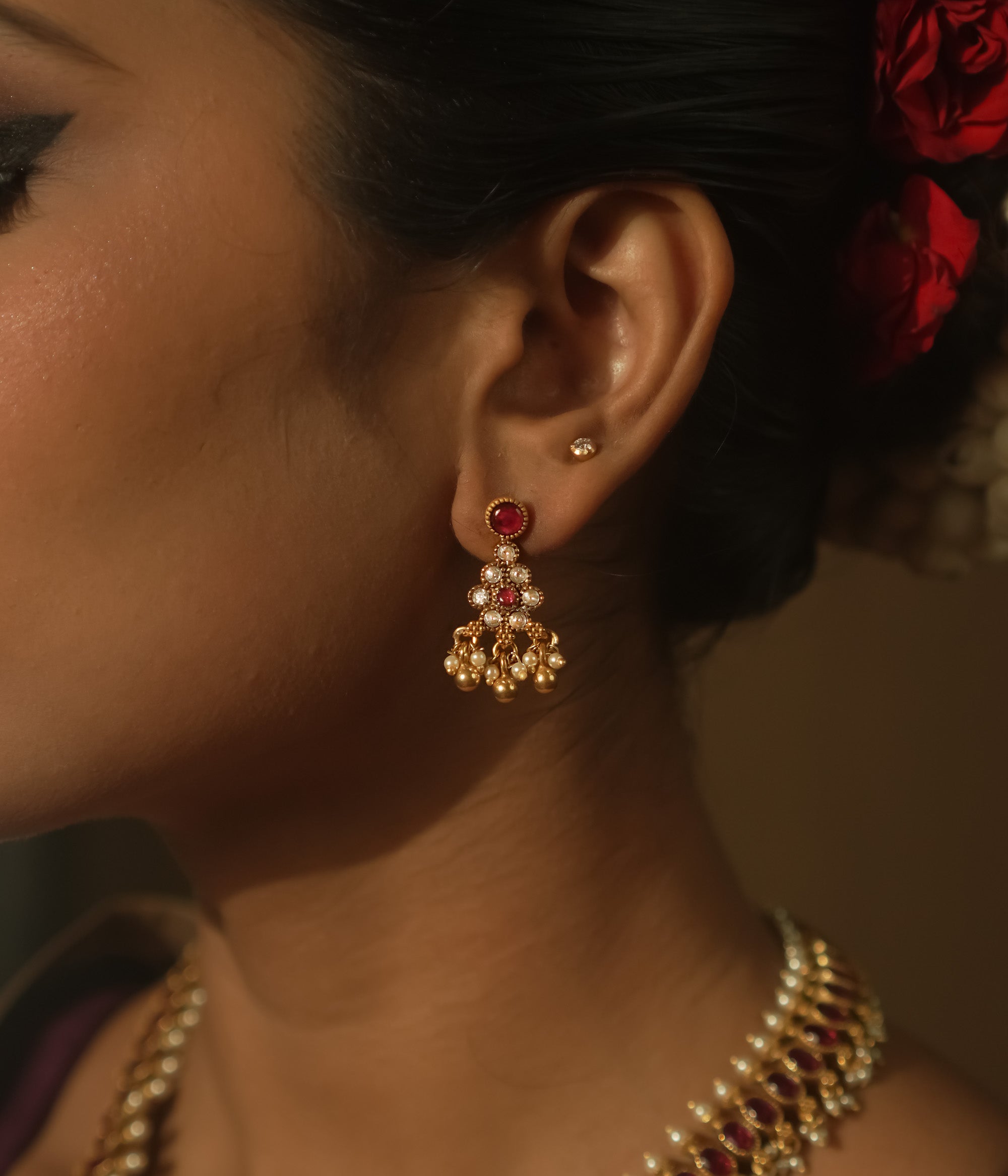 A red ear stud paired with a dangling gold jhumka with beads and gems.