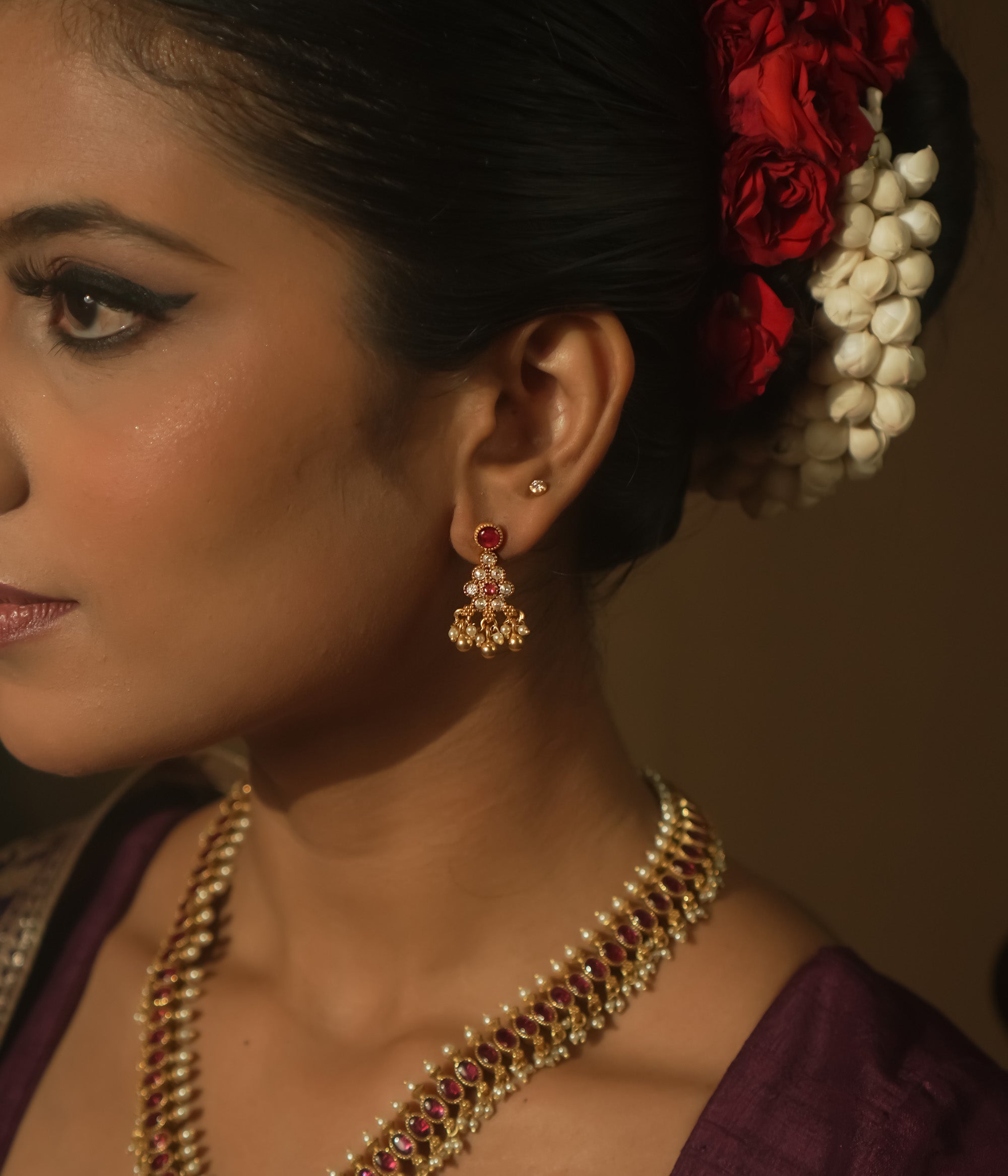 A red ear stud paired with a dangling gold jhumka with beads and gems.