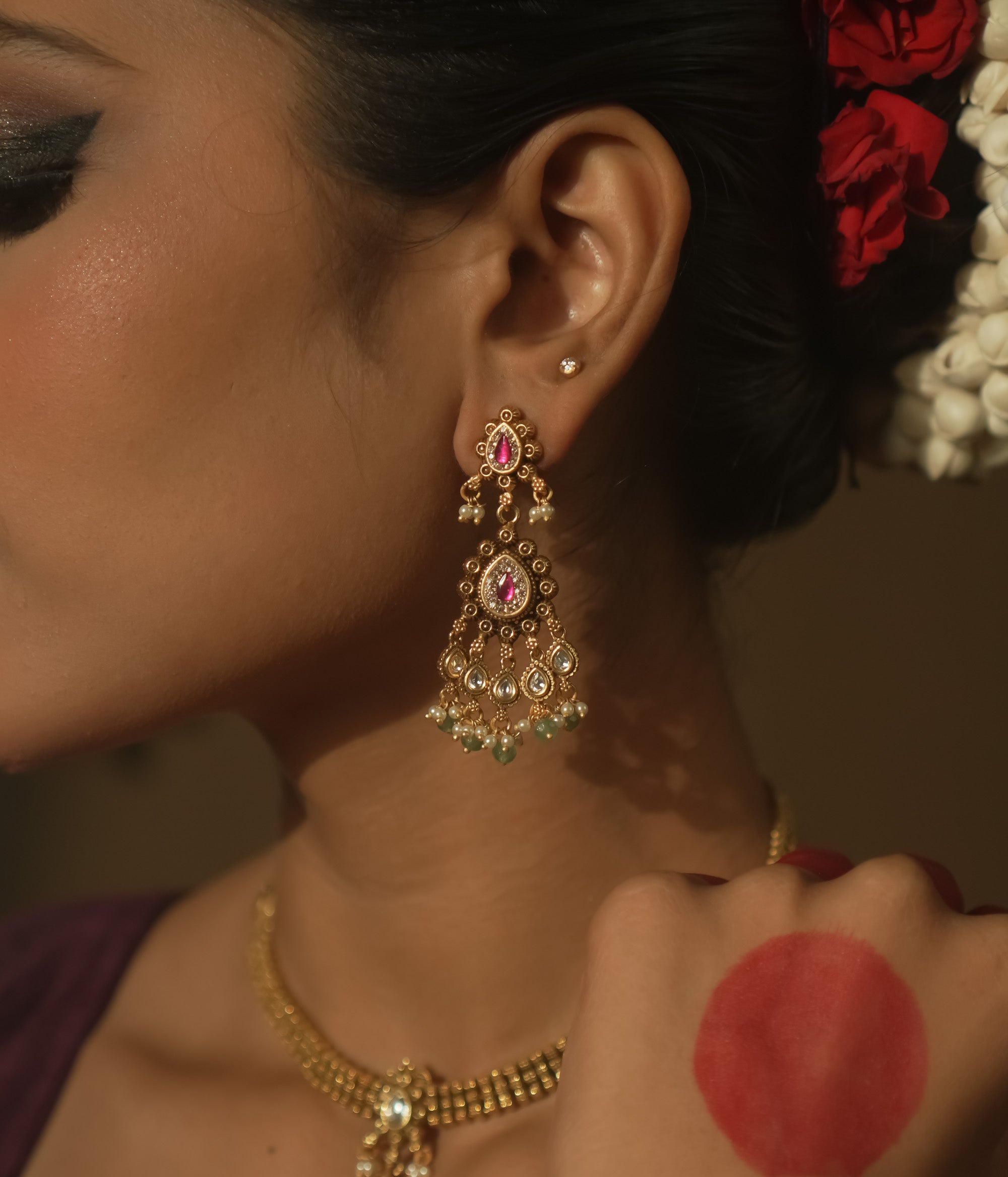 Tiered earrings with pink gemstones, clear Kundan stones, and emerald drops.