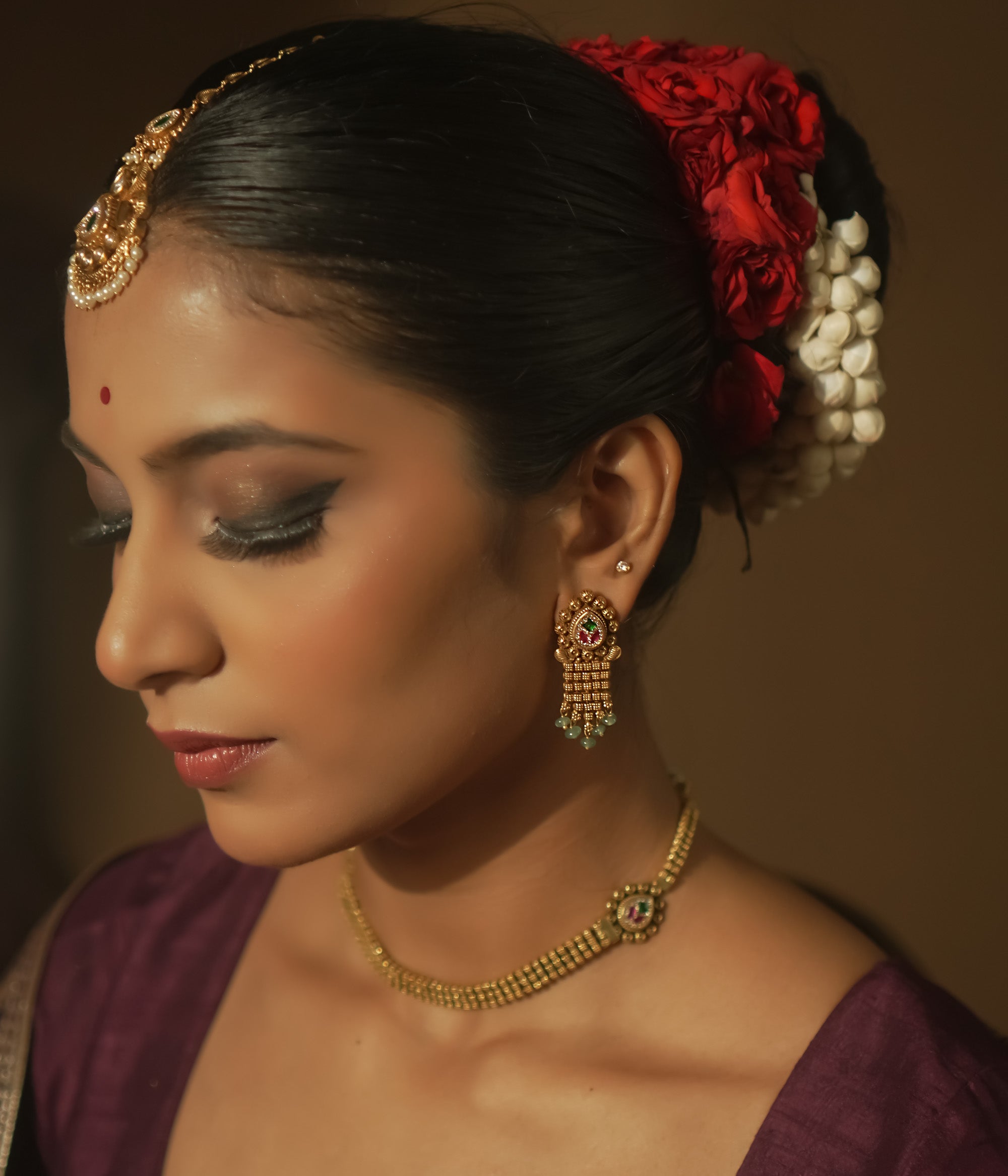 Gold earrings with teardrop charms, vibrant Kundan, and emerald fringes.