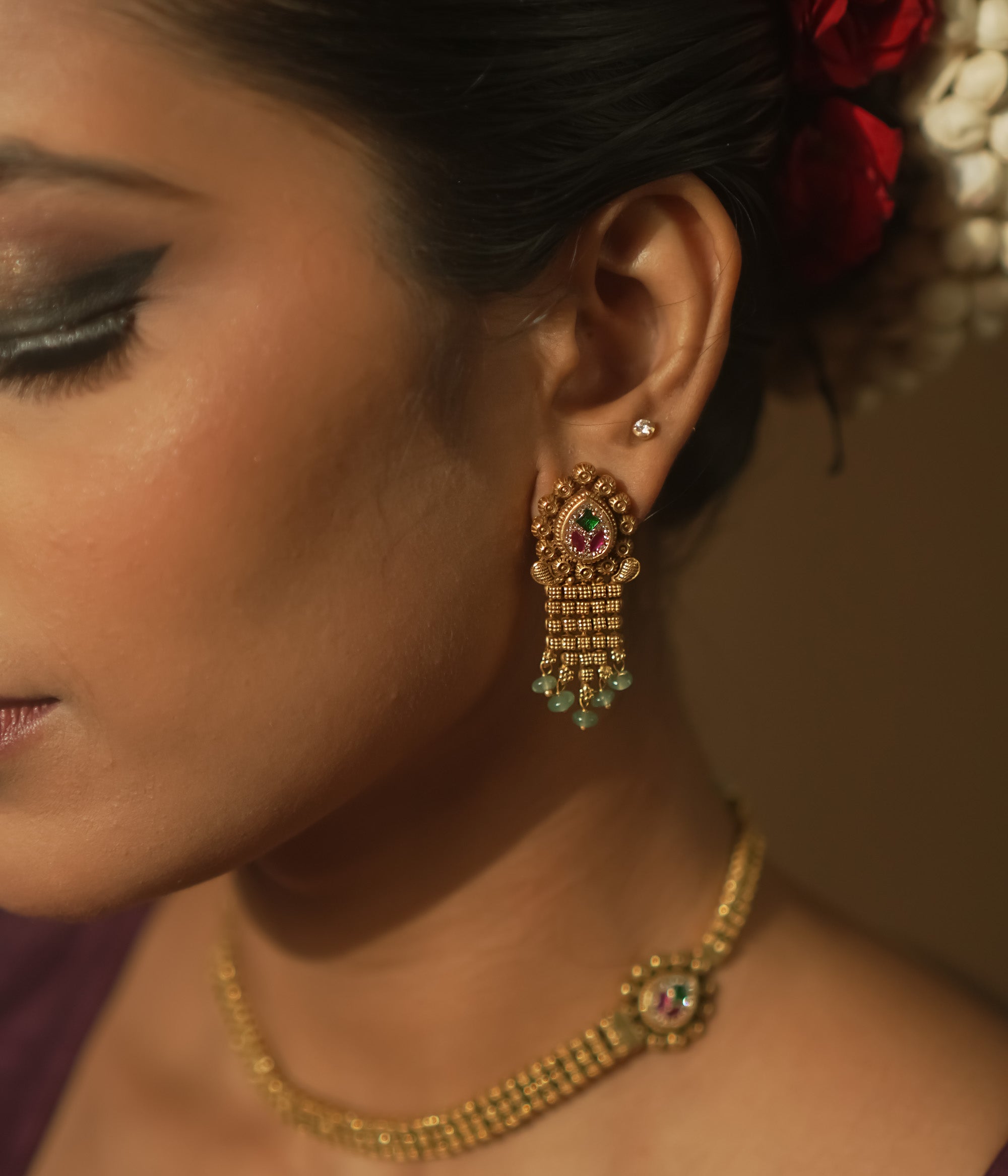 Gold earrings with teardrop charms, vibrant Kundan, and emerald fringes.
