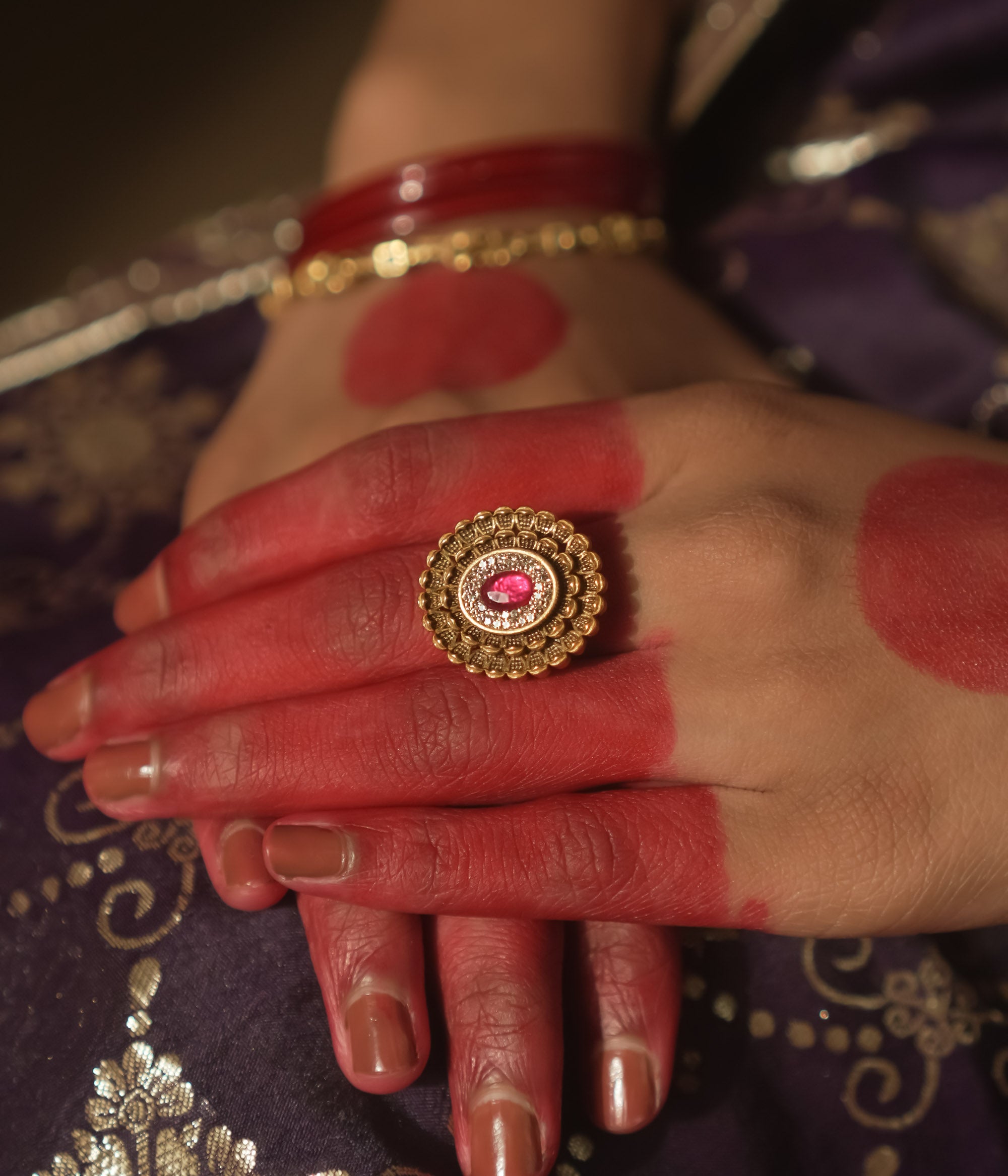 Gold ring with an antique design, tiny gems, and a central crimson jewel.