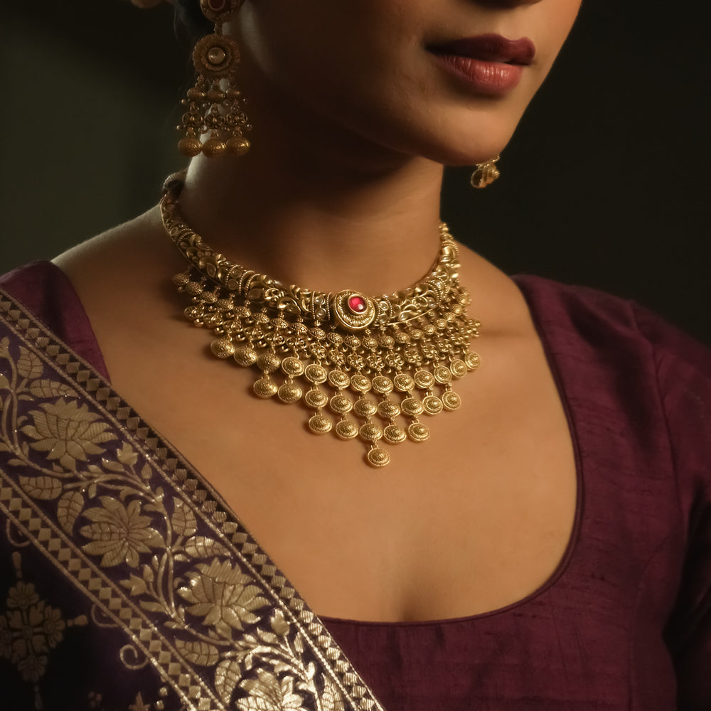 Gold necklace with dangling coin motifs and a central pendant with red gems.