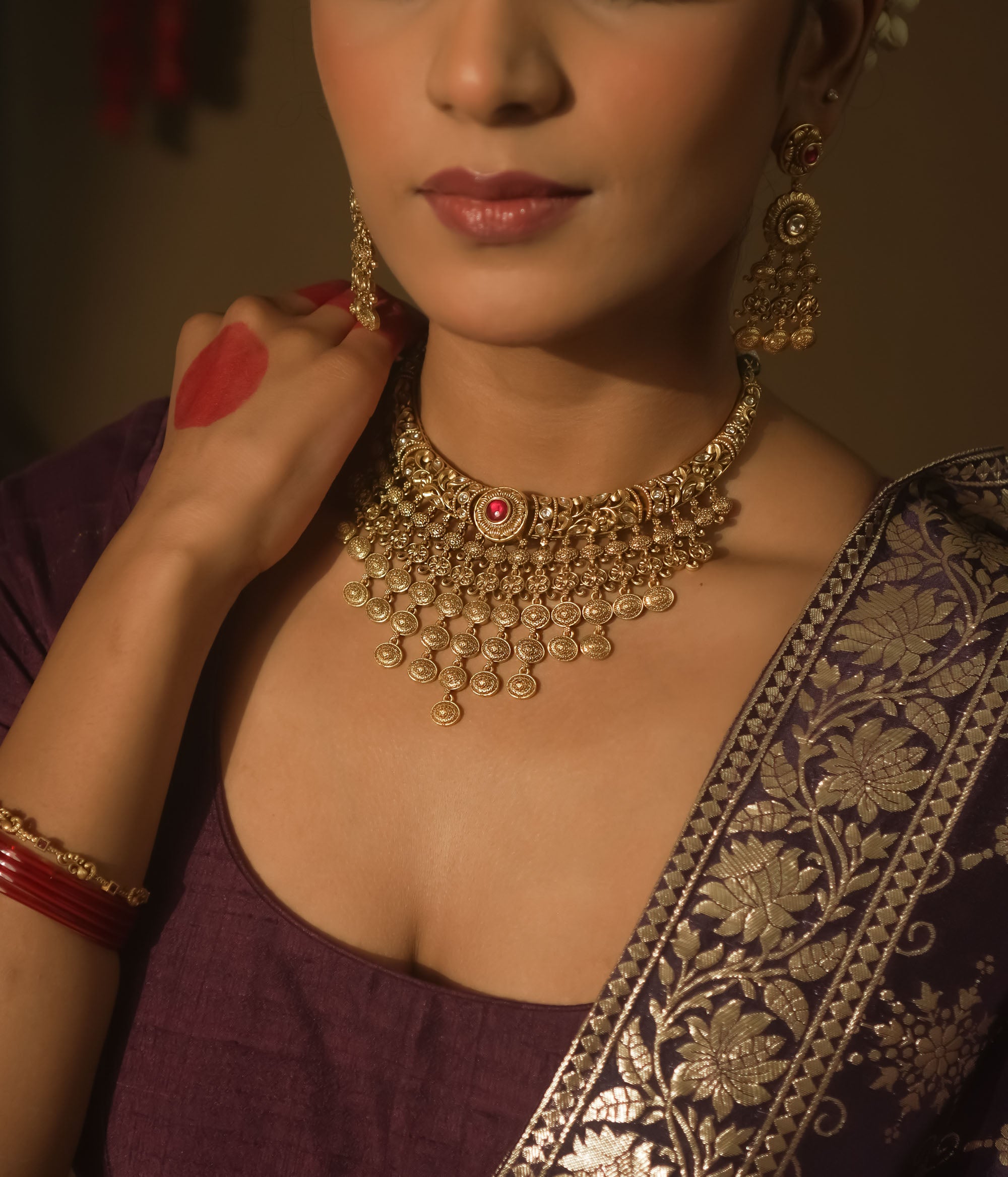 Gold necklace with dangling coin motifs and a central pendant with red gems.