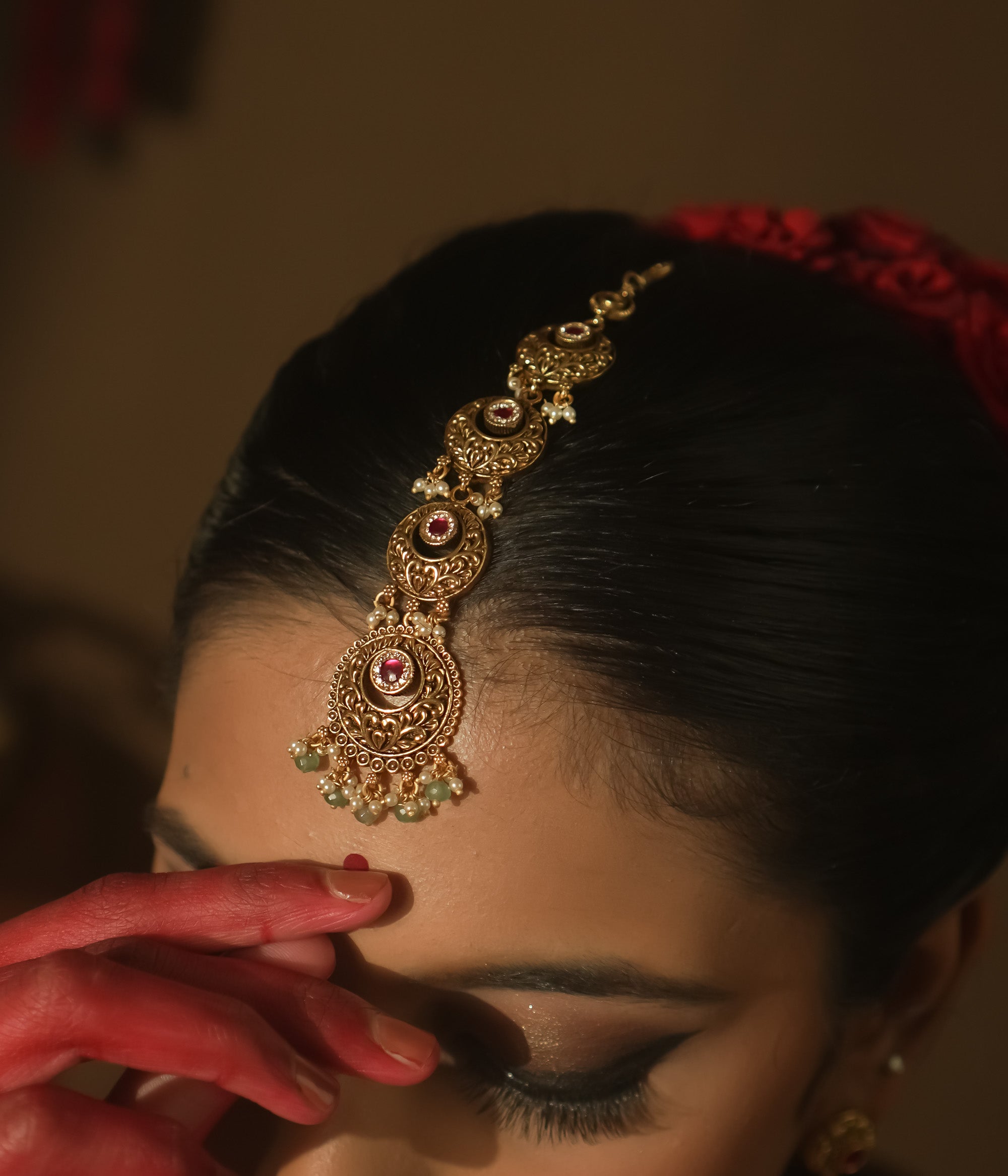Gold-plated silver maangtika with red and green gemstones and dangling green beads.