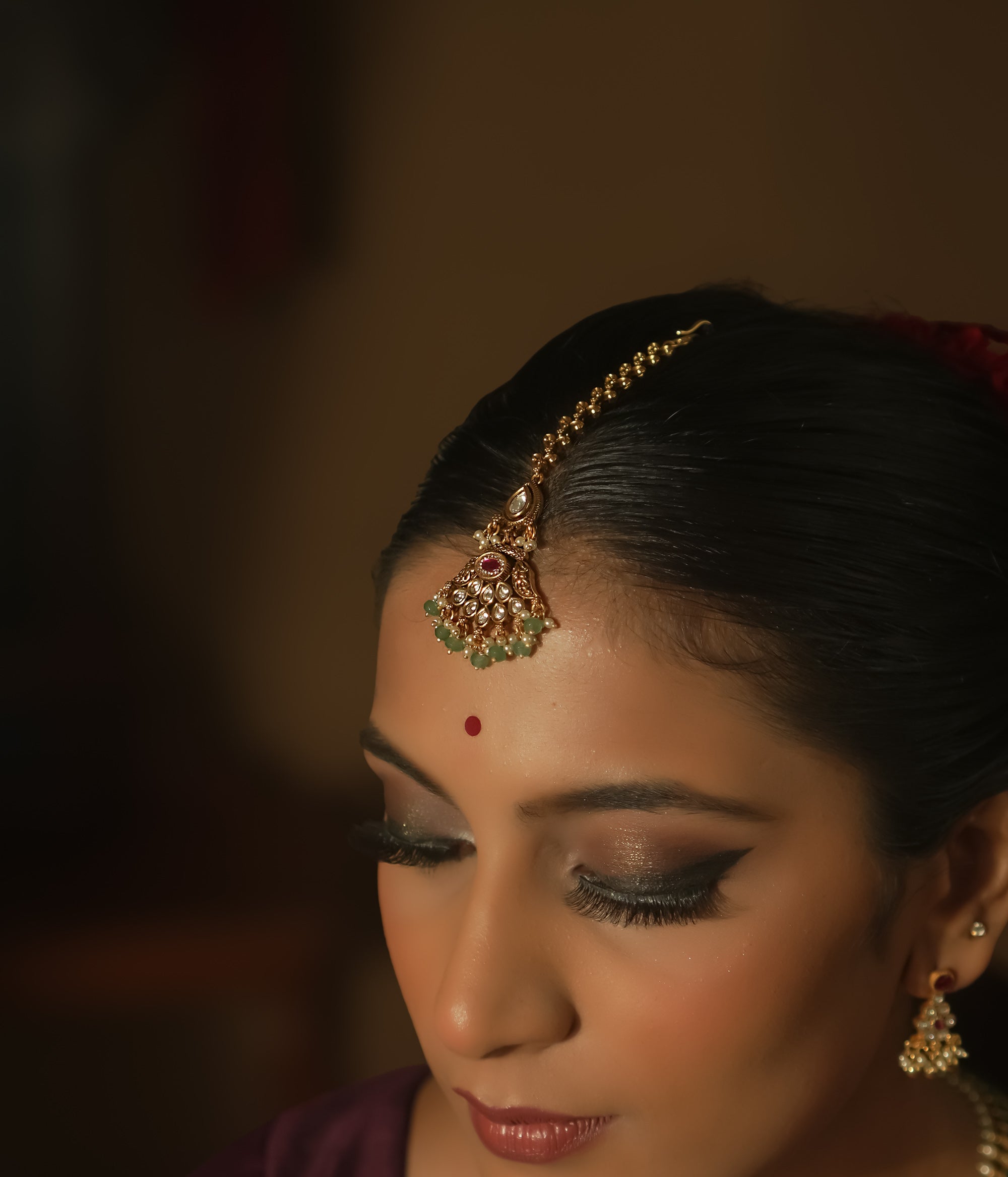 Gold maangtika with a central red gem, emerald beads, and a delicate chain.