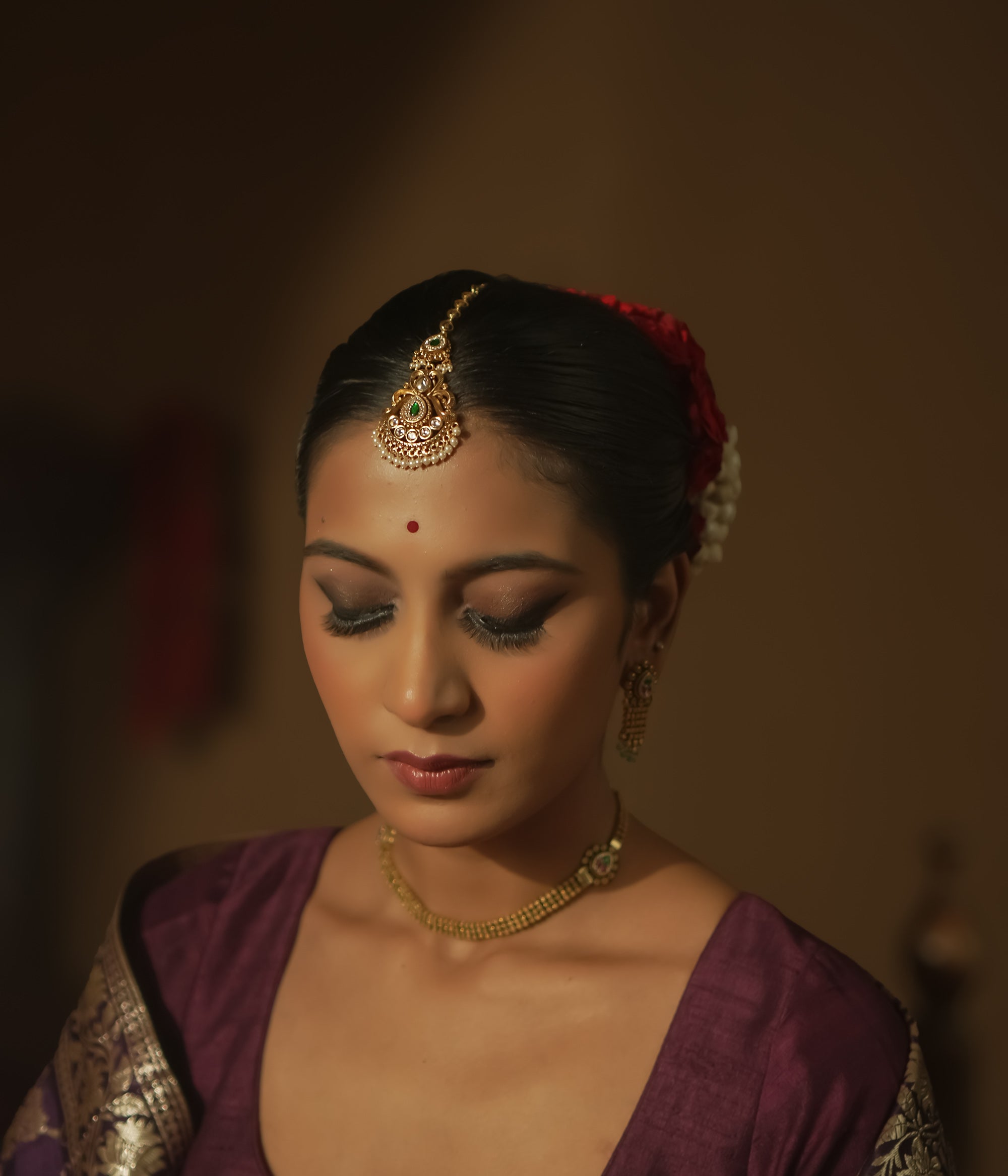 Gold maangtika with a central green teardrop gemstone, pearls, and red floral motifs.