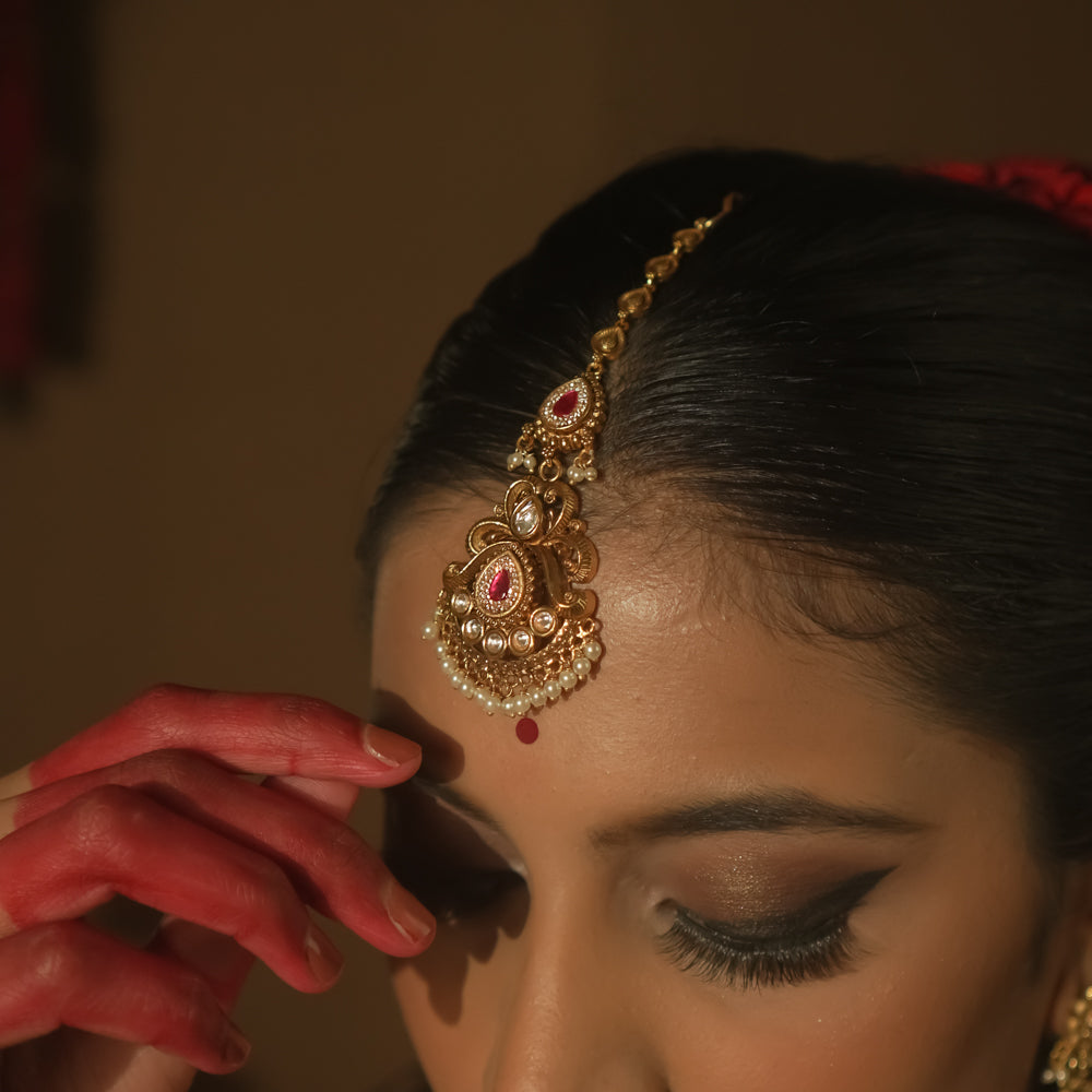 Maangtika with gold swirls, cultured rubies, pearls, and a dangling red gemstone.