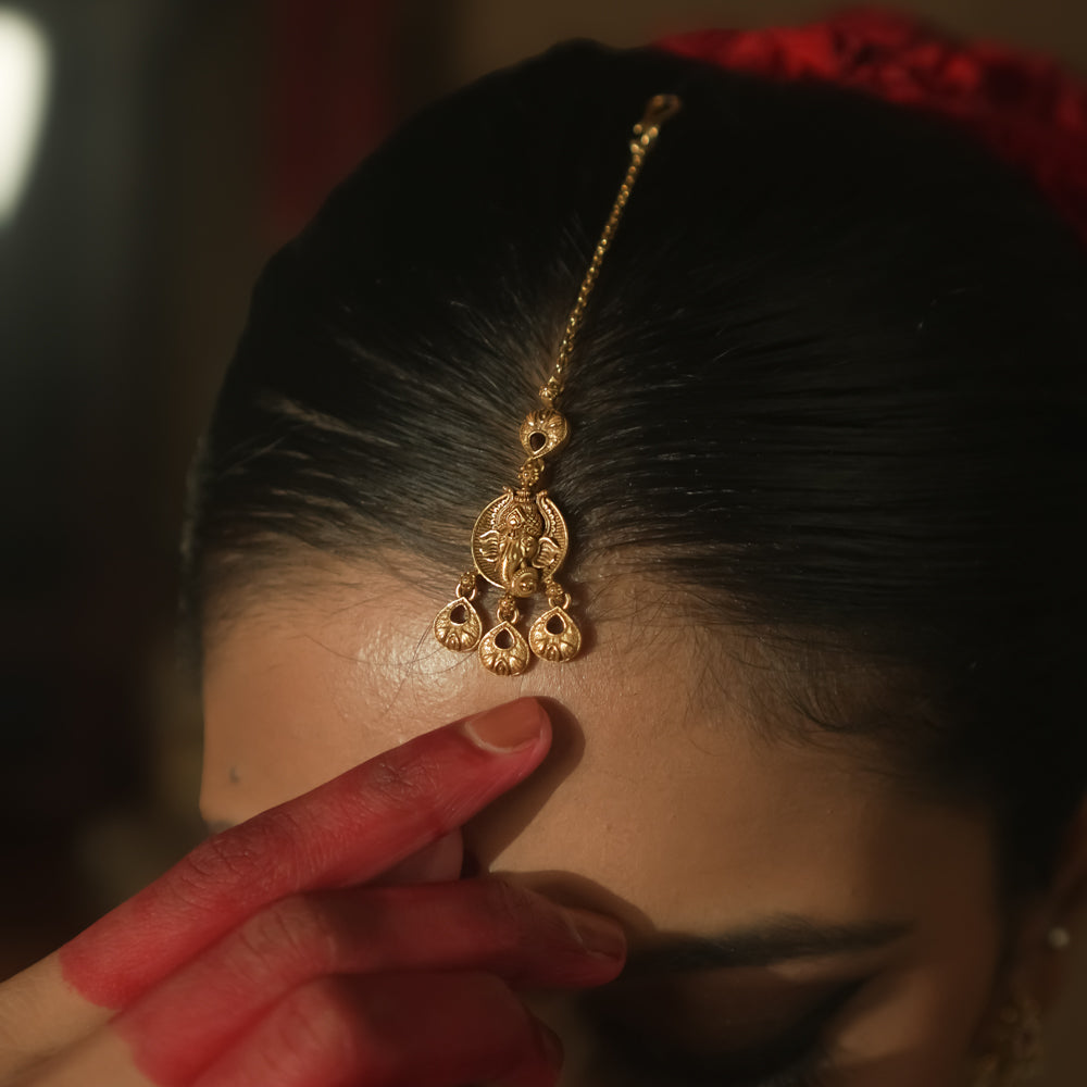 Gold maangtika with a delicate chain and ornate dangling teardrops.