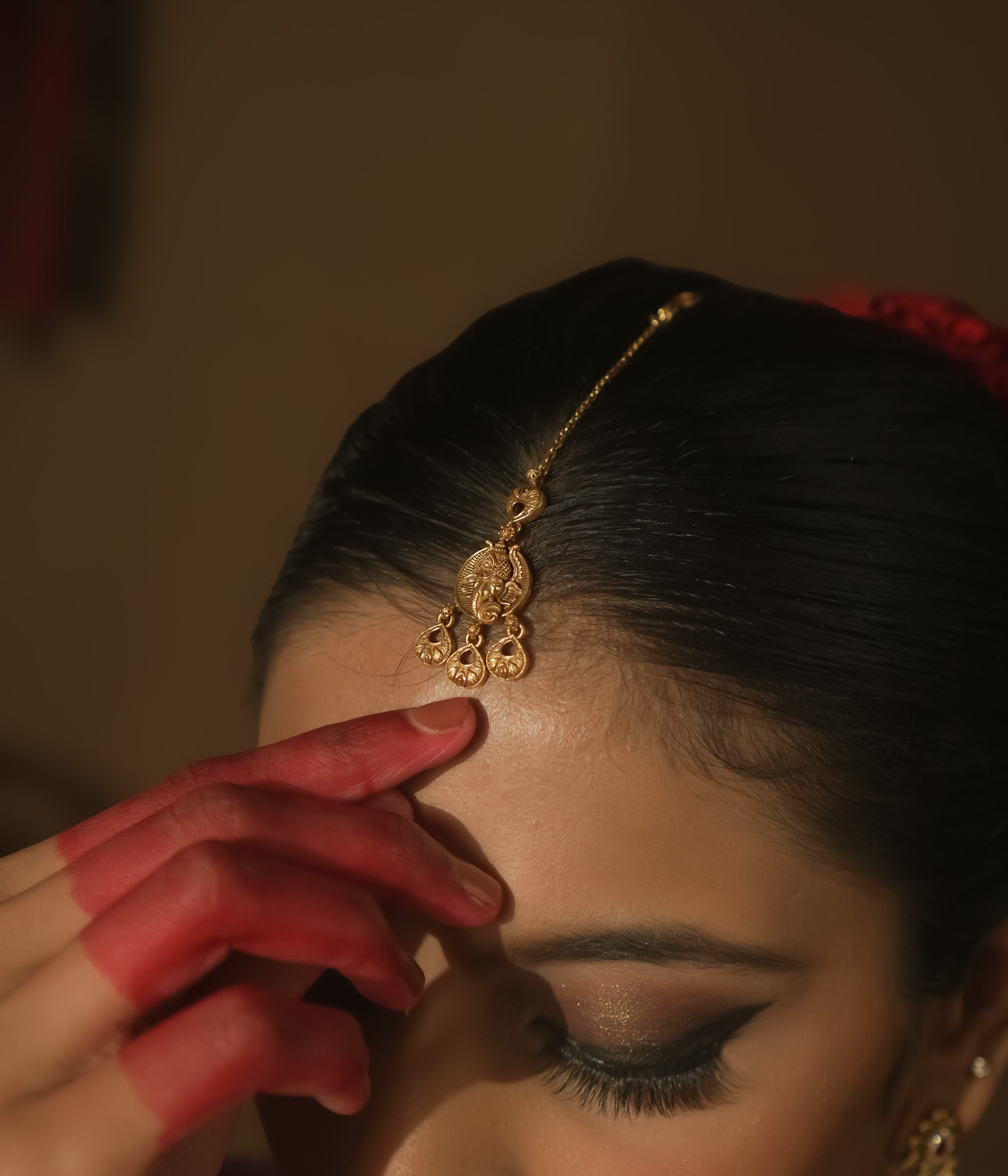Gold maangtika with a delicate chain and ornate dangling teardrops.