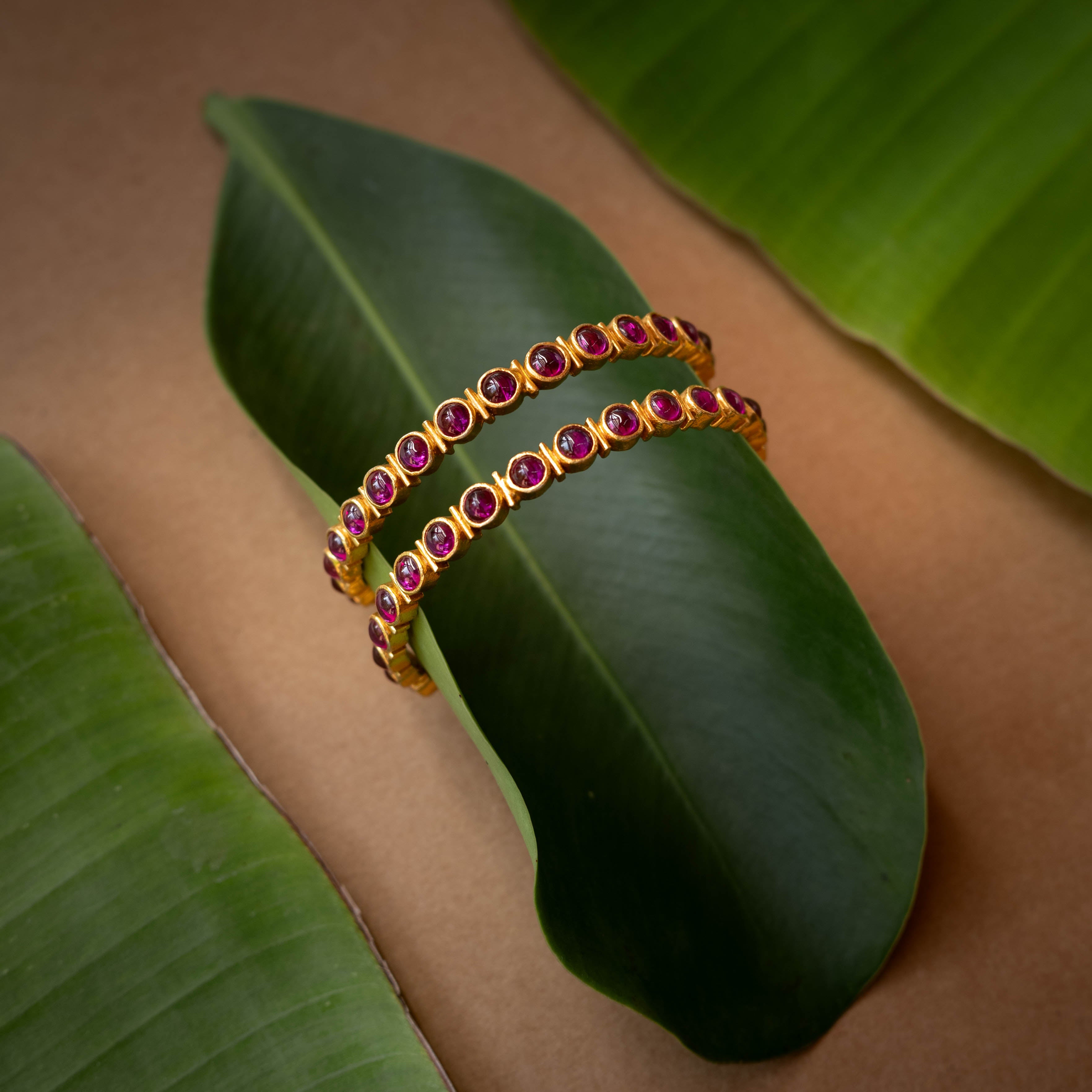 A gold-toned hinged bangle with a row of red stones in the center.
