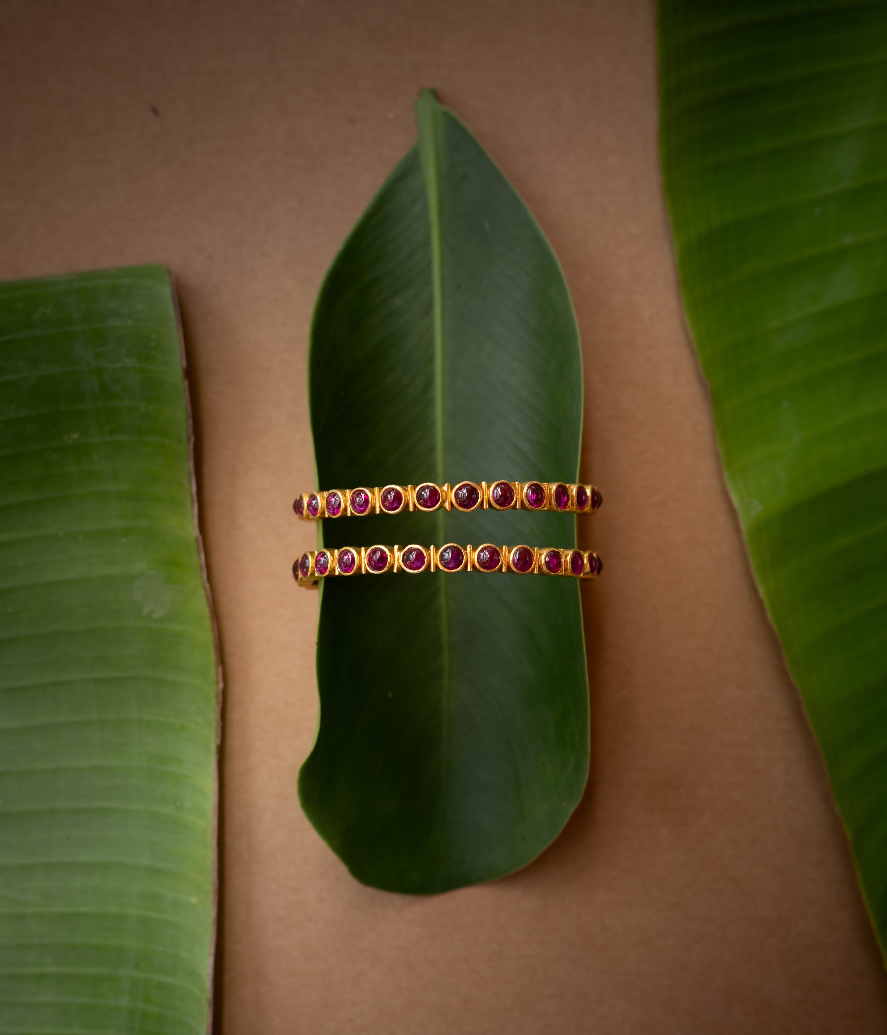 A gold-toned hinged bangle with a row of red stones in the center.
