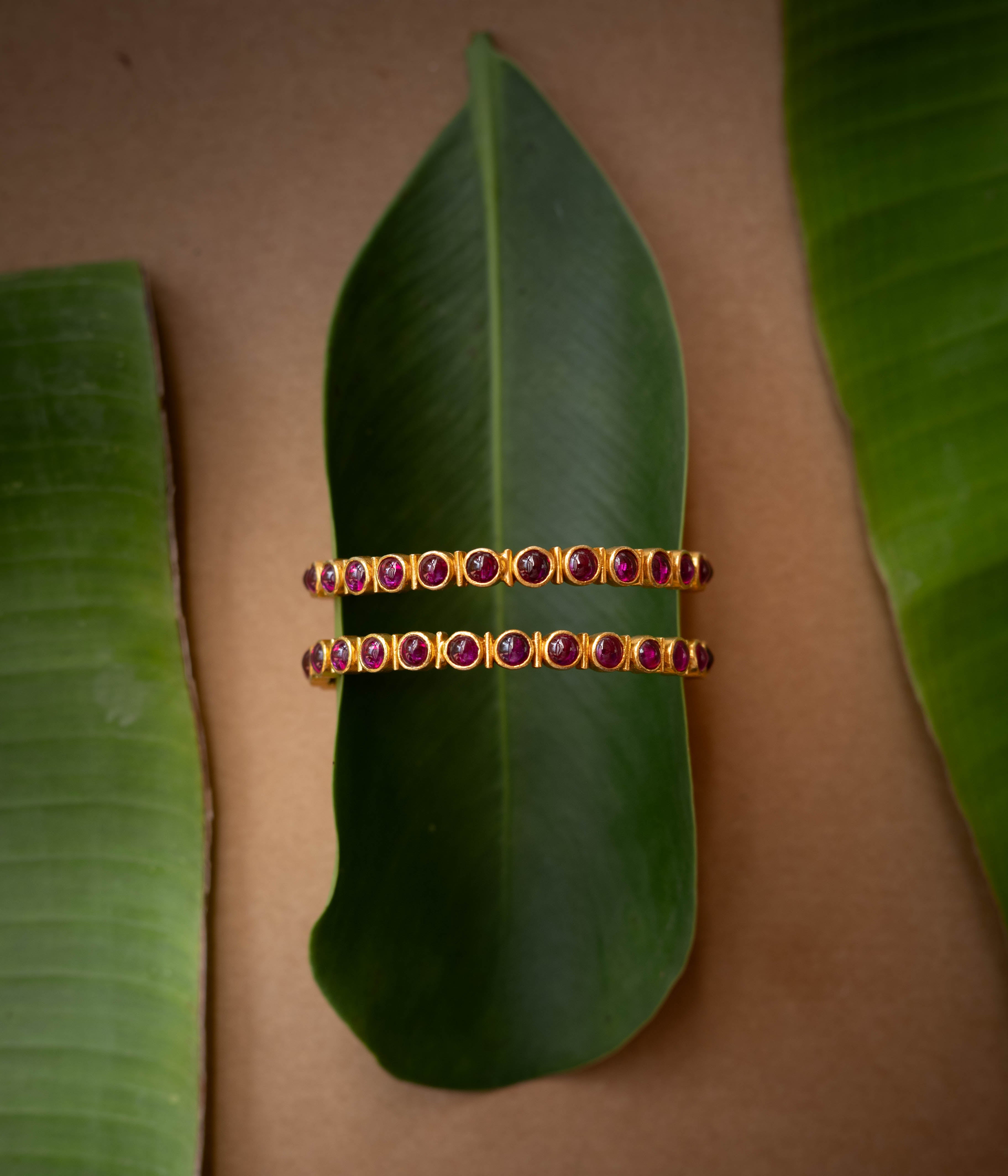 A gold-toned hinged bangle with a row of red stones in the center.
